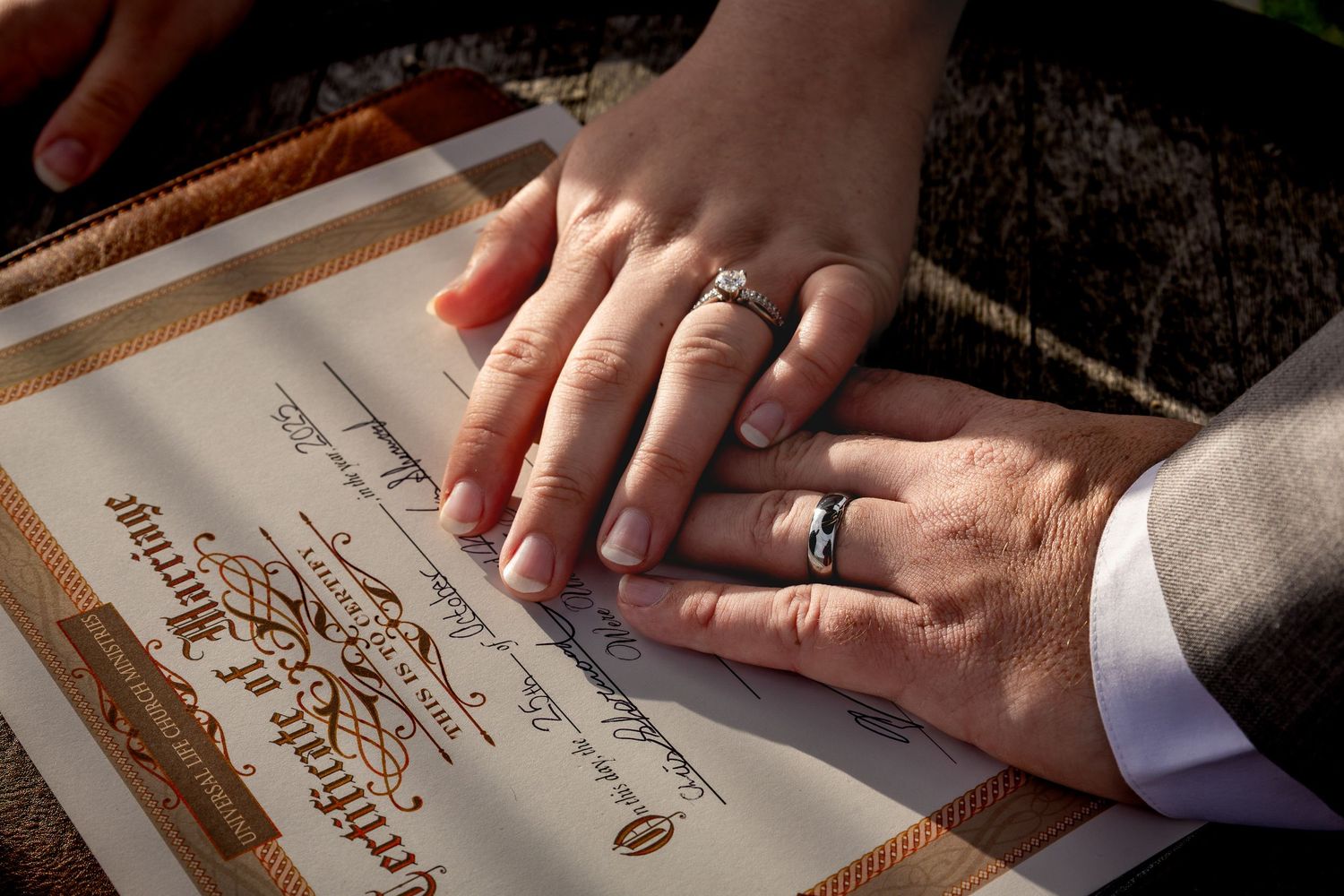 Close-up of hands signing wedding documents with rings visible.