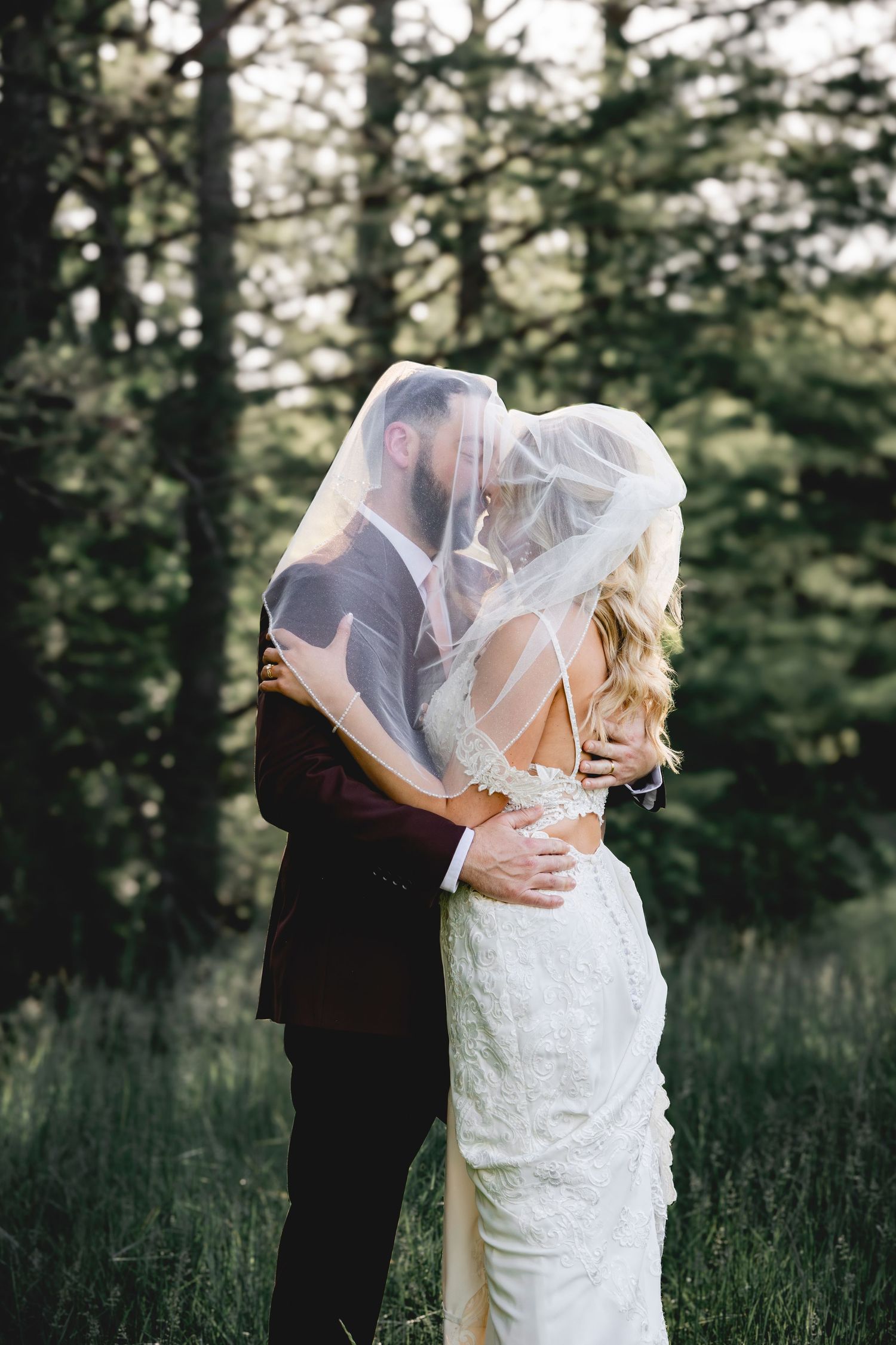 A romantic wedding moment captured in a wooded setting with soft natural lighting.