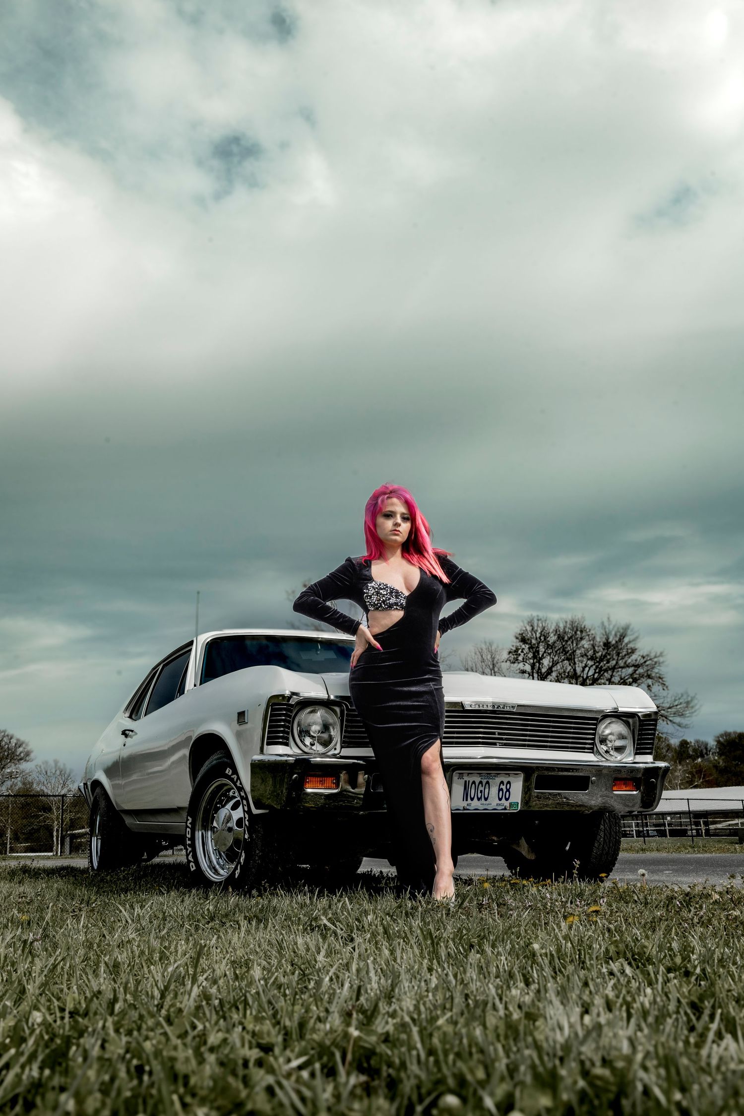 Vintage white Chevrolet photographed with model in black dress against moody sky.