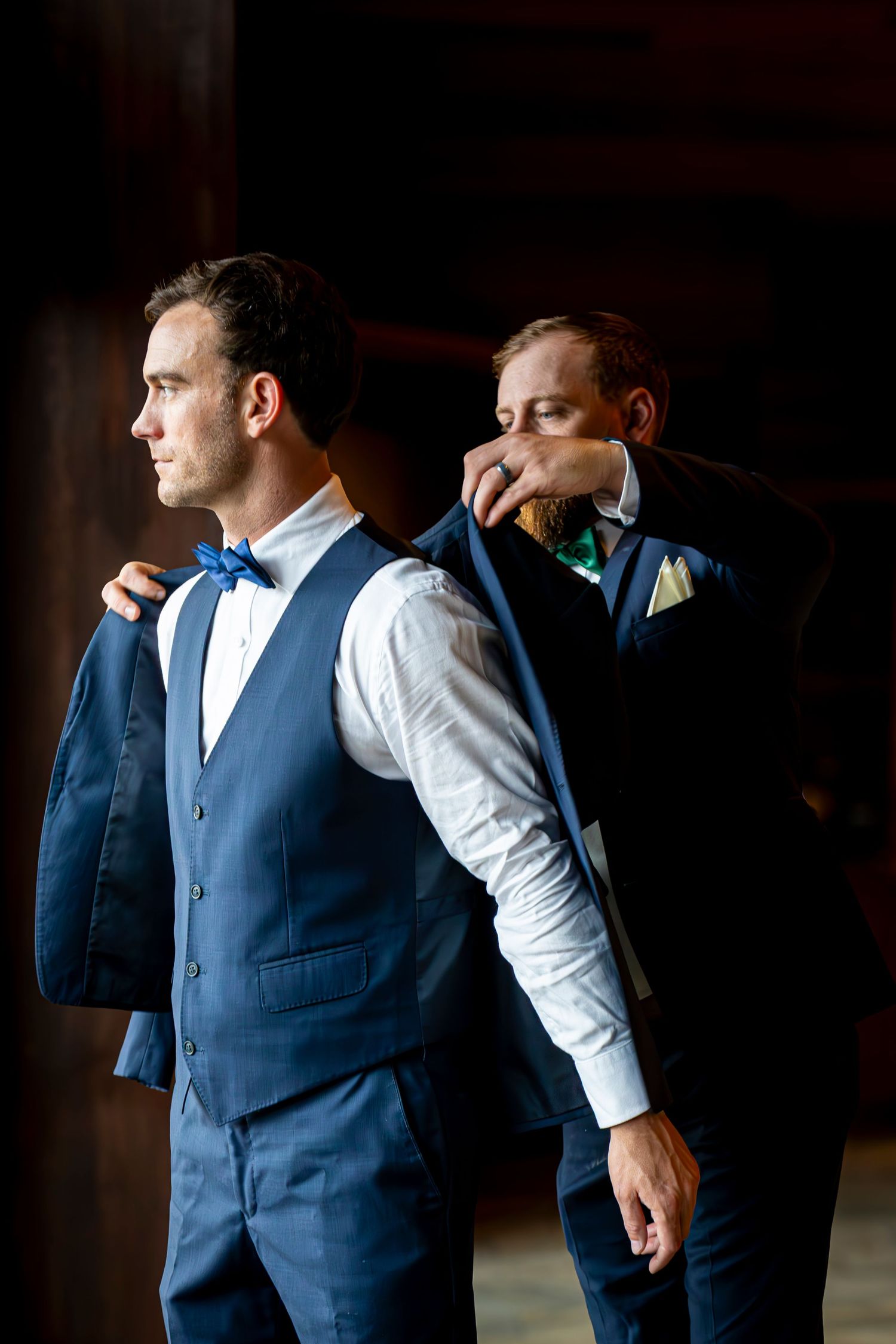 A groom adjusts his tie while getting ready in dramatic lighting.
