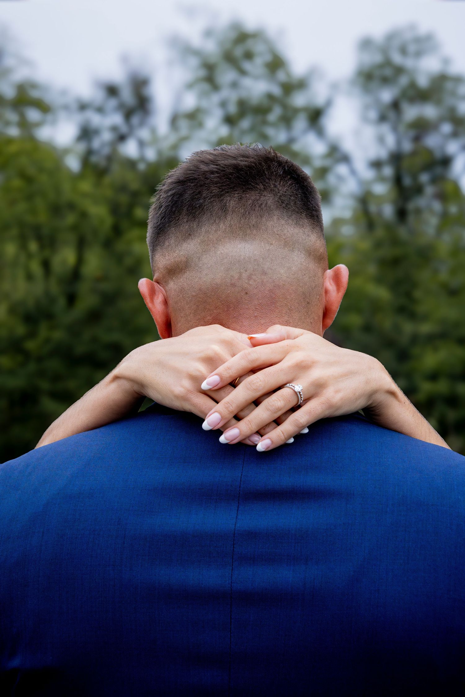 Close-up of hands with wedding ring resting on blue suit jacket.
