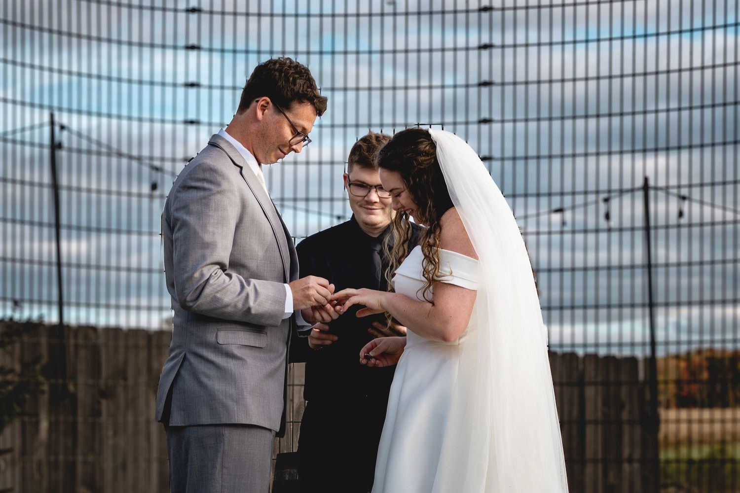 Wedding ceremony moment under metal gazebo structure with string lights.