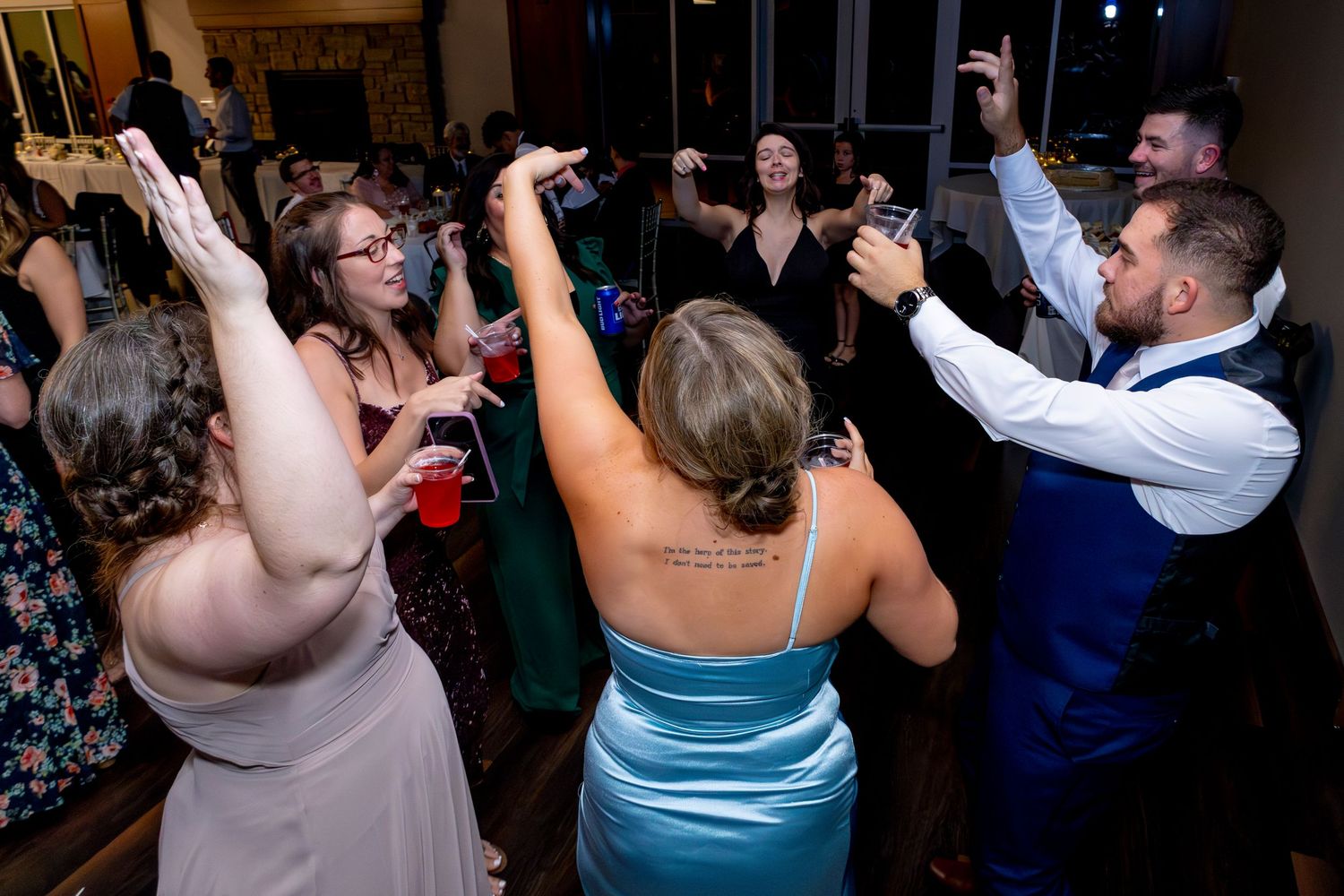 Wedding reception guests dance with raised arms on dark dance floor.