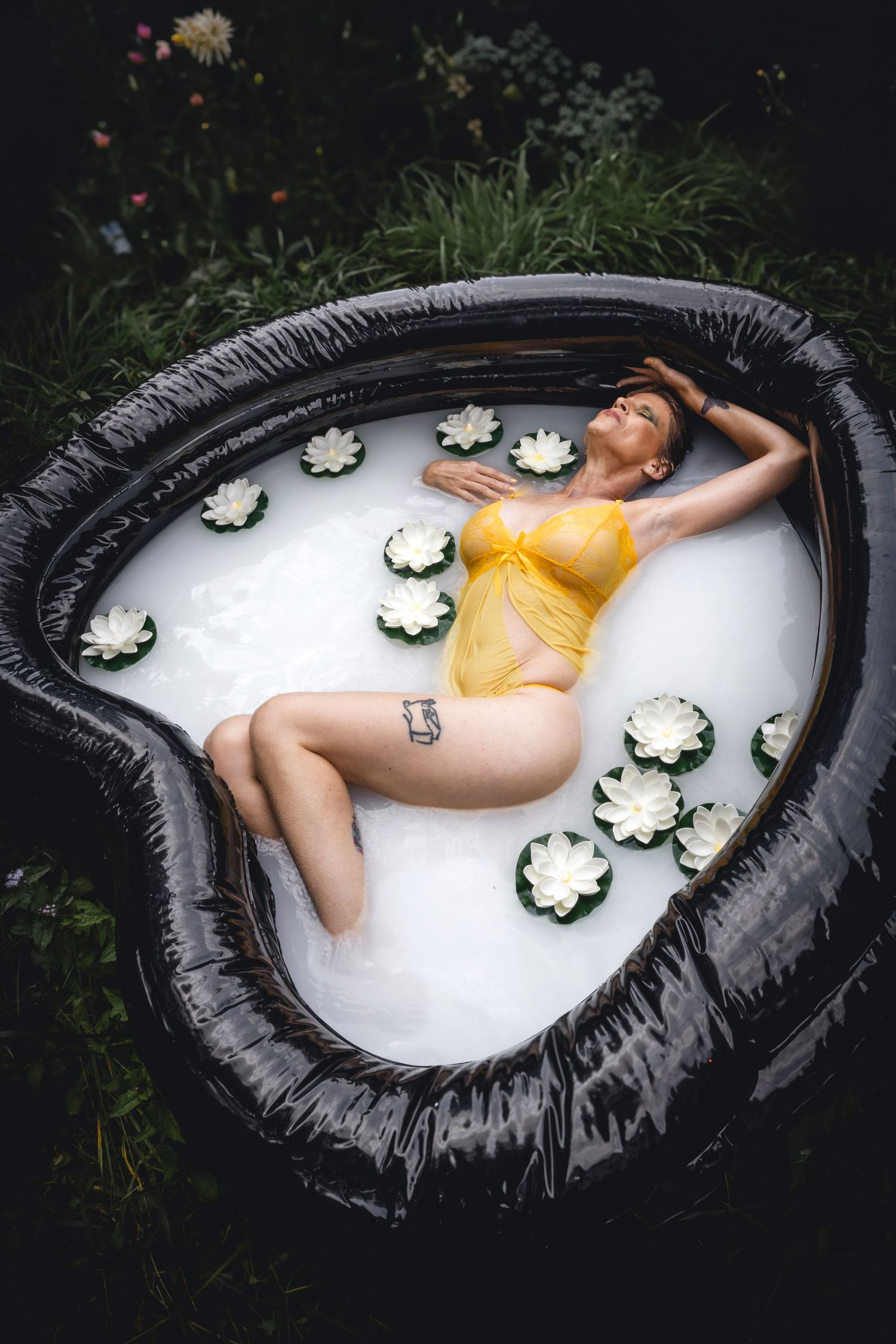 Artistic photo of someone in yellow lingerie lying in heart-shaped pool with floating flowers.
