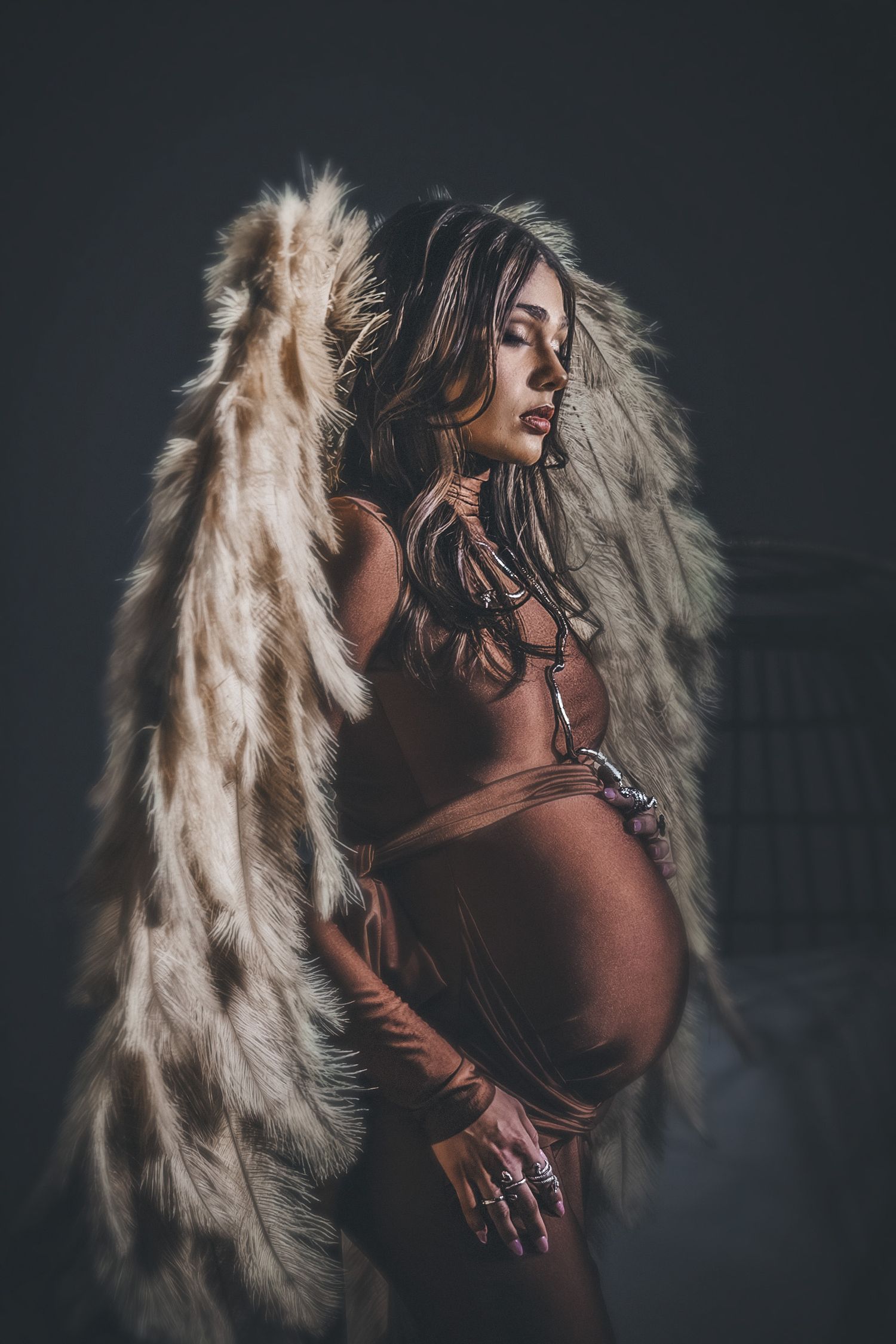 Artistic portrait series featuring dramatic lighting and ethereal white wings against dark background. Maternity.
