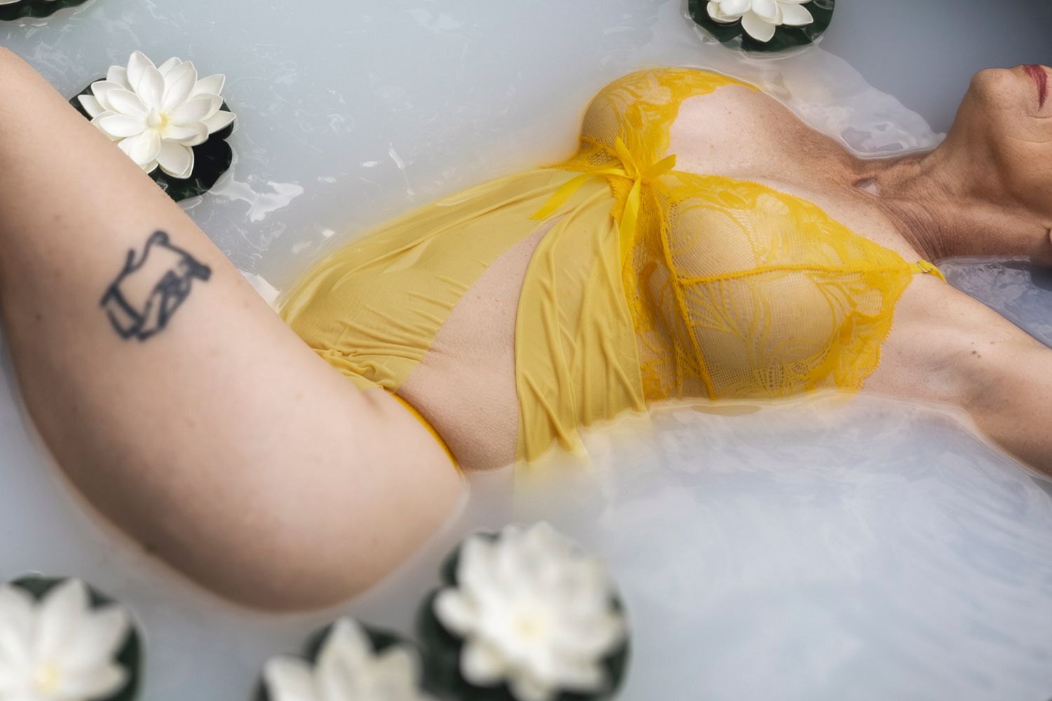 Close-up detail of yellow fabric and white flowers in milky bath water.