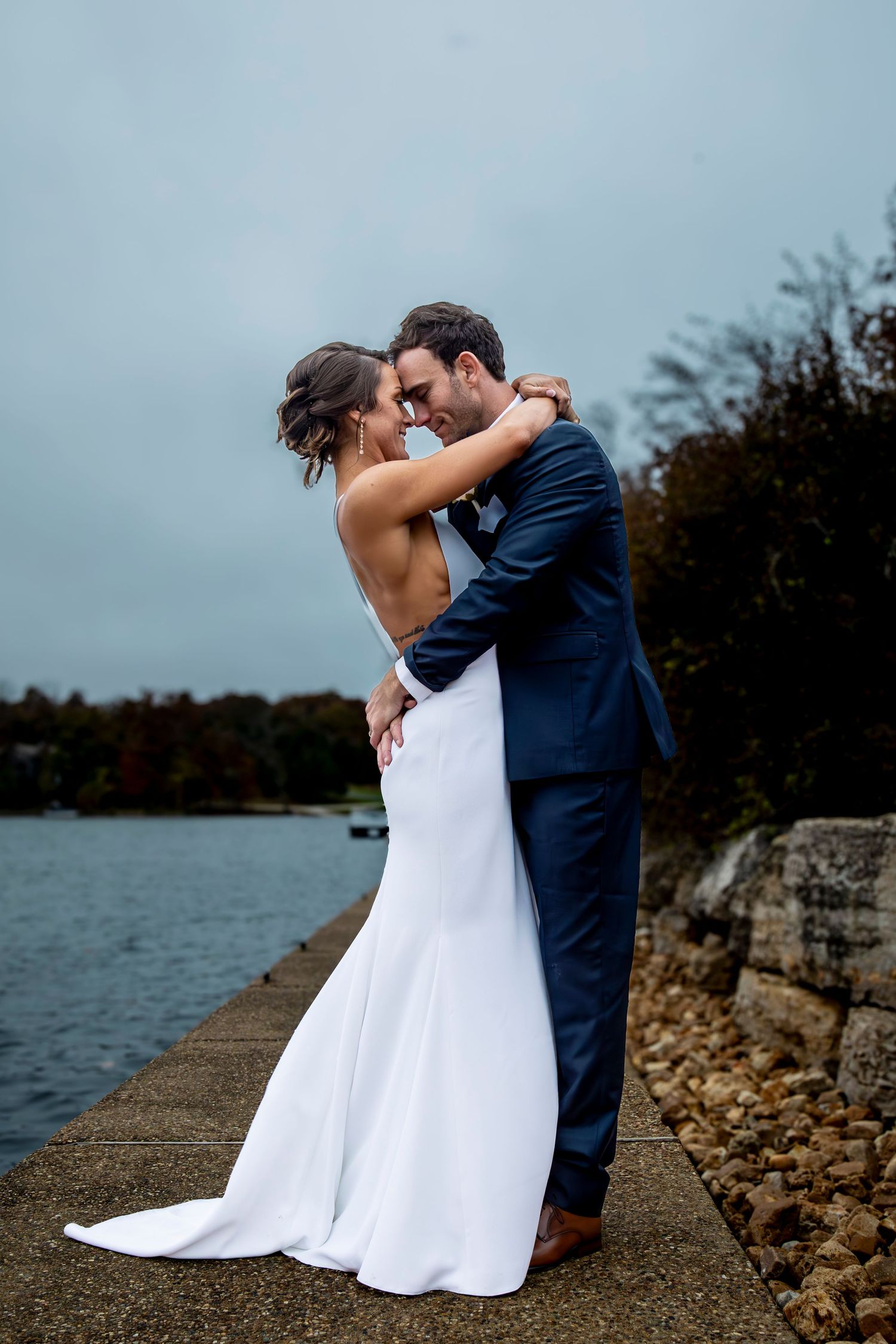 Romantic wedding couple embracing on stone path by the water.