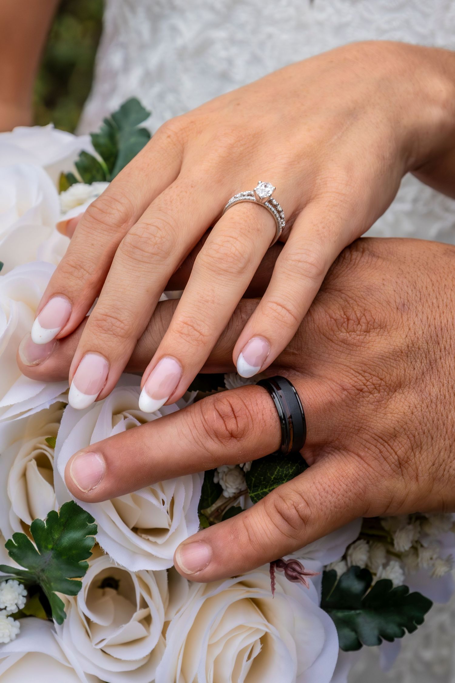 Close-up of wedding rings and hands on white rose bouquet.