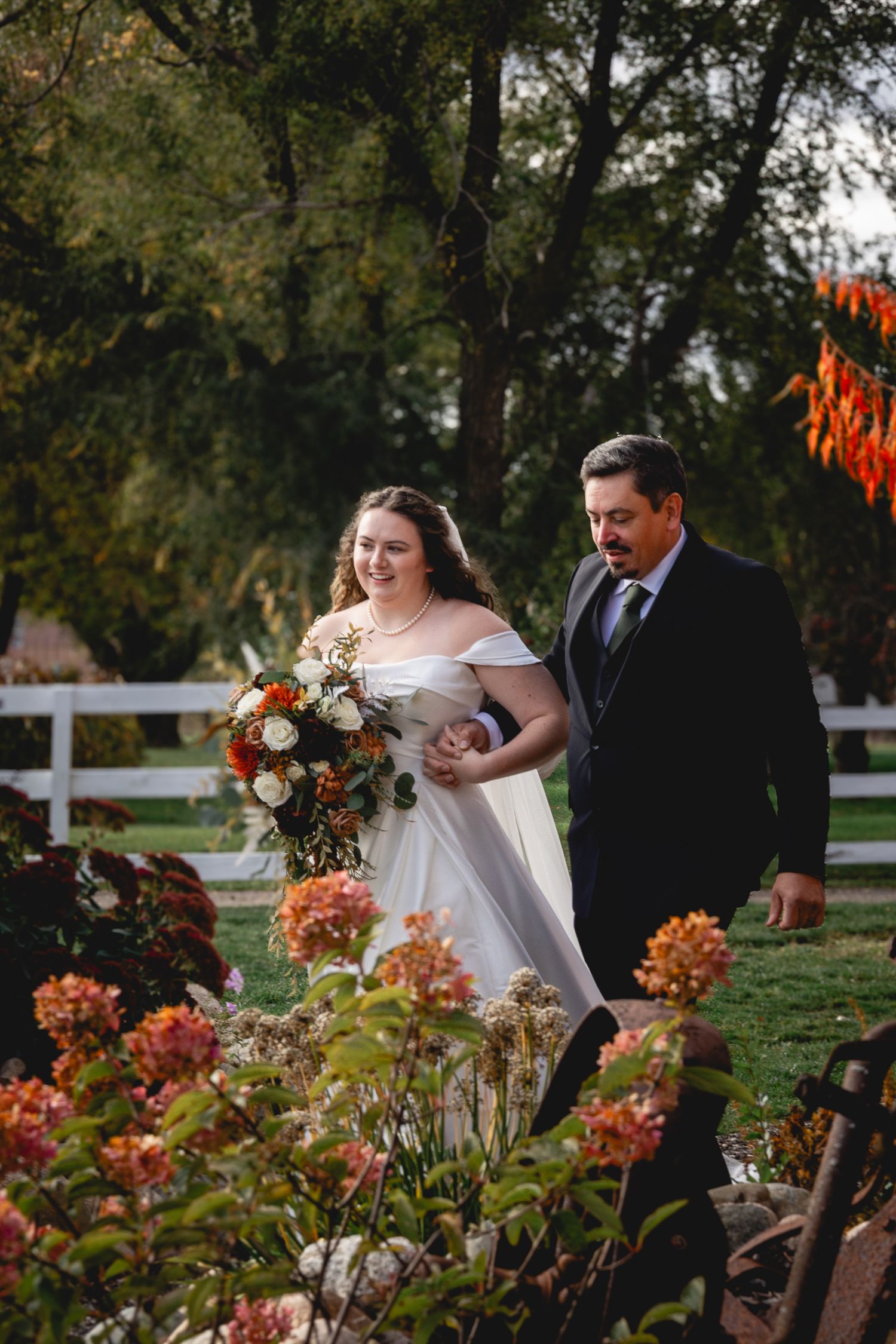 Autumn wedding scene with orange flowers and white fencing in a garden setting.