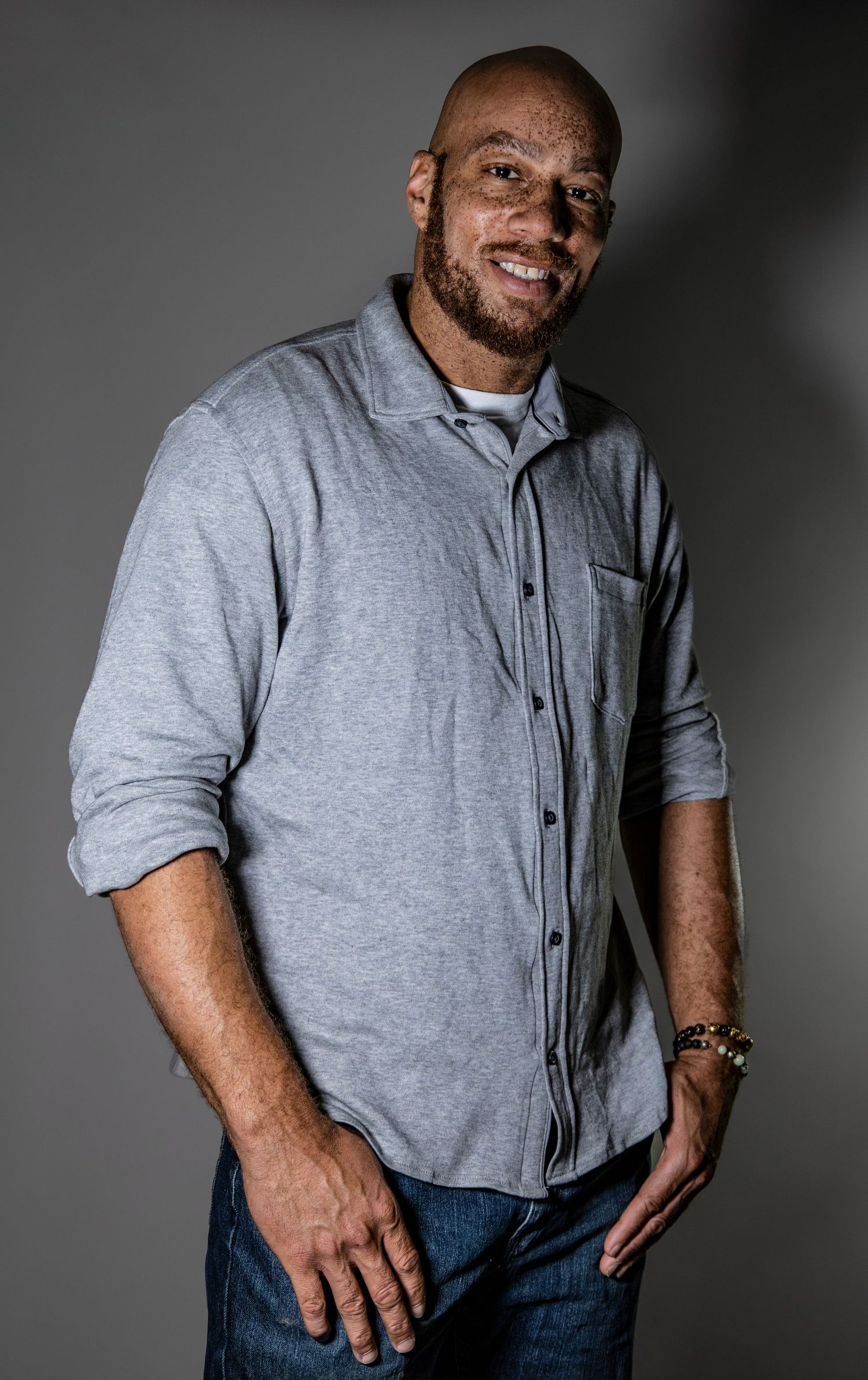 Professional studio portrait of person in casual grey button-up shirt against dark background.