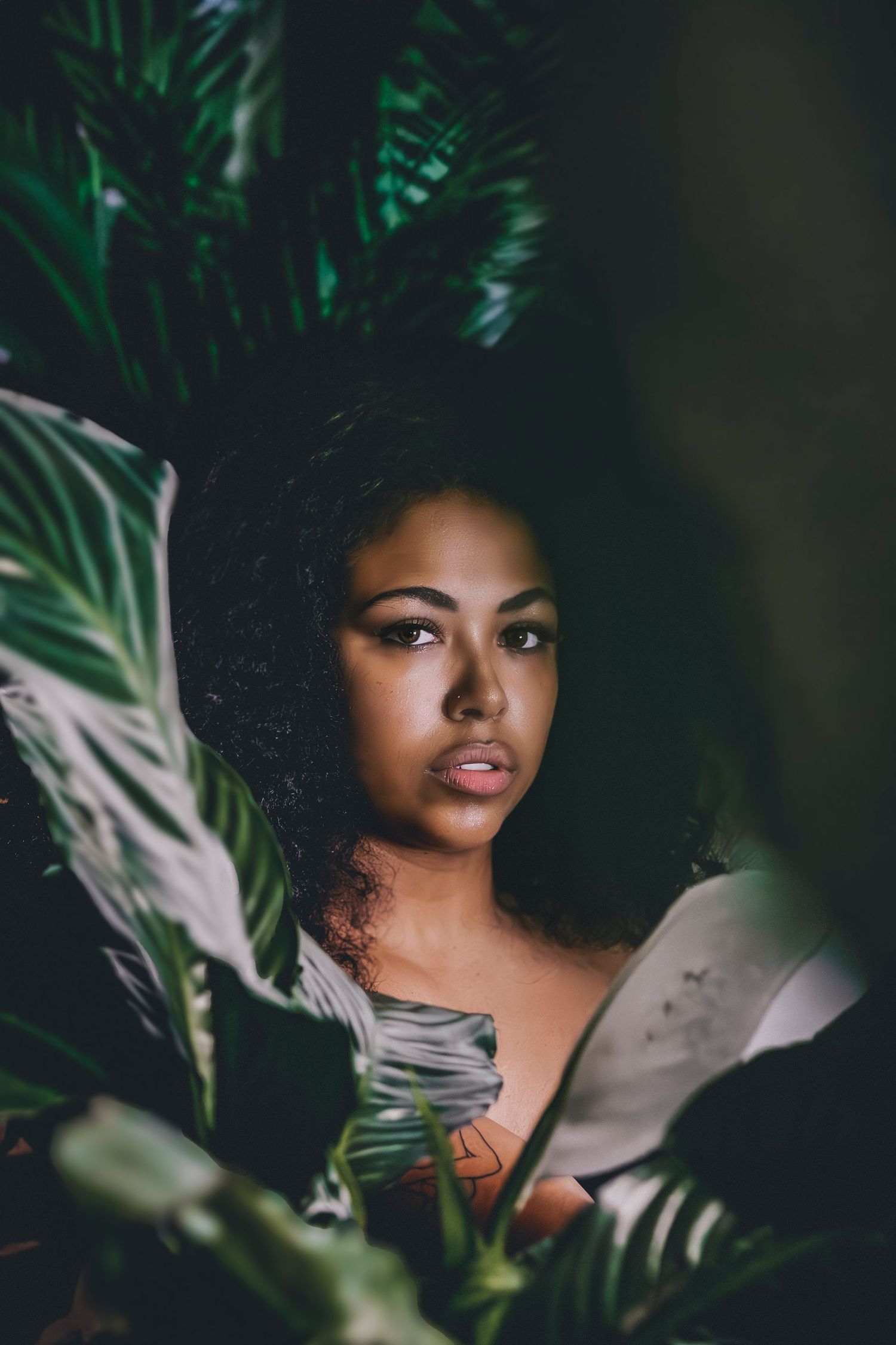 Close-up portrait through tropical leaves with soft natural lighting and lush green foliage.