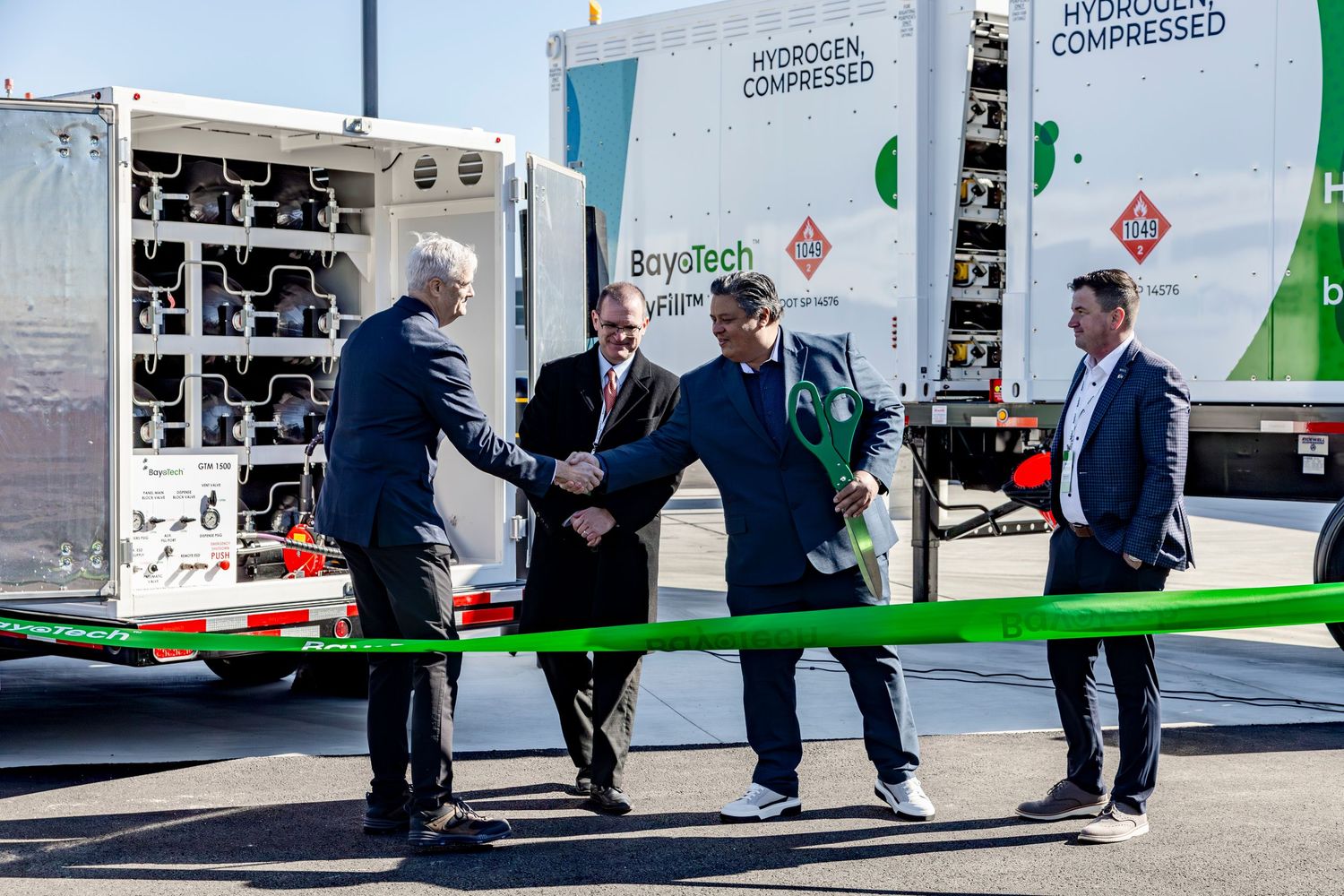 Business people cutting ribbon at ceremonial opening event with industrial equipment.