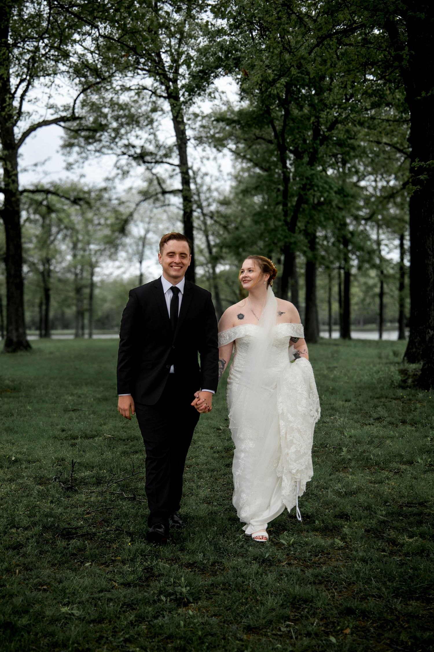 Wedding couple walking through a wooded area in formal attire.