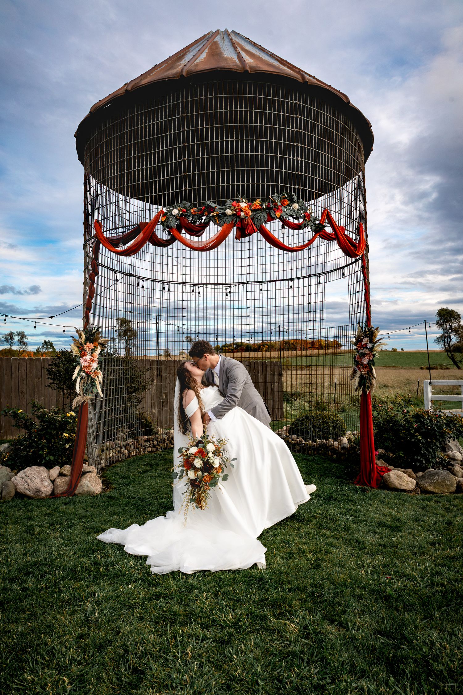 Wedding ceremony setup under a gazebo with floral decorations against a cloudy sky.