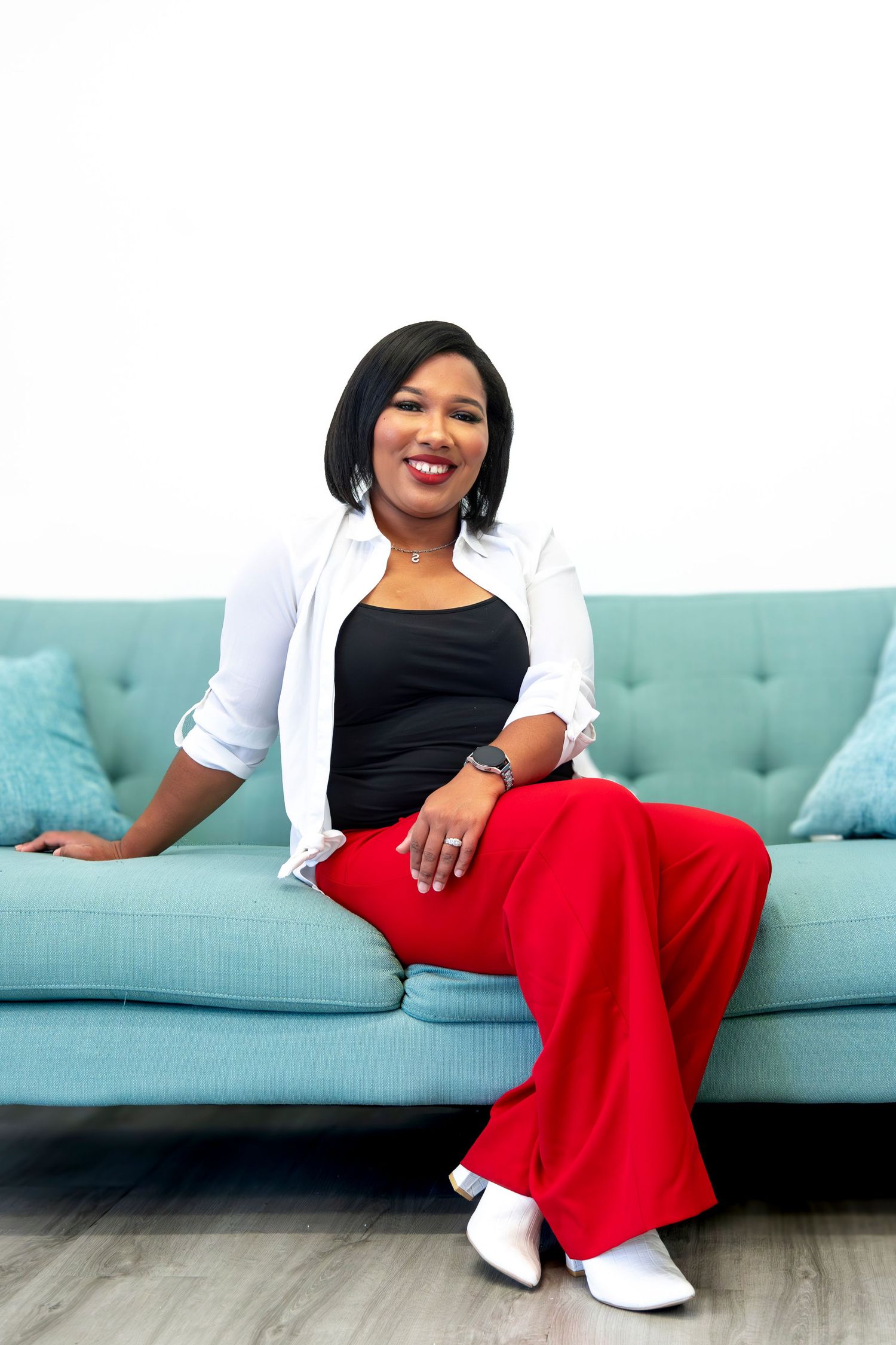 Person in black and white outfit relaxes on turquoise couch in bright studio setting. Headshot.