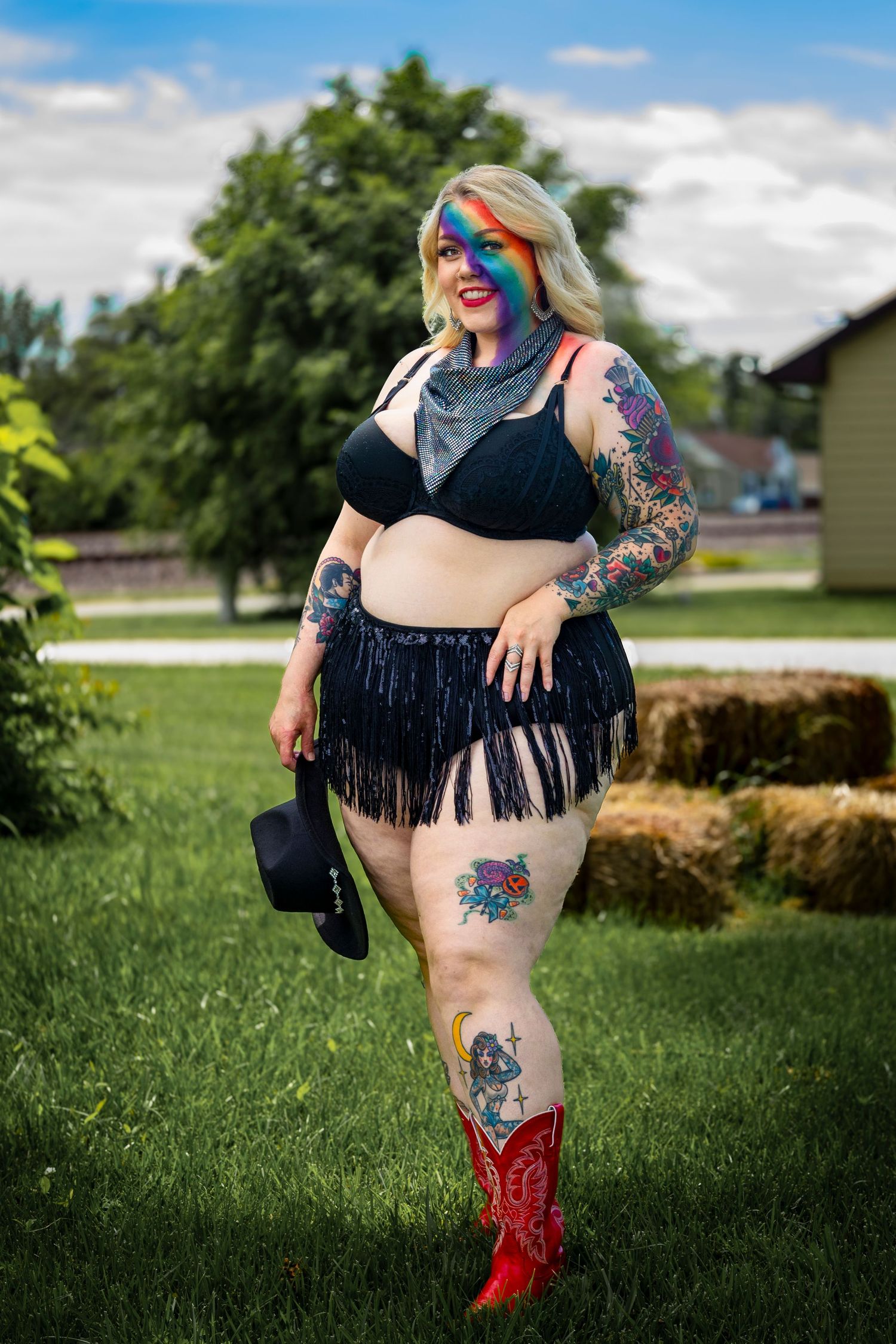 Artistic outdoor photoshoot featuring colorful tattoos, fringe details, and red boots on grassy backdrop. Pride.