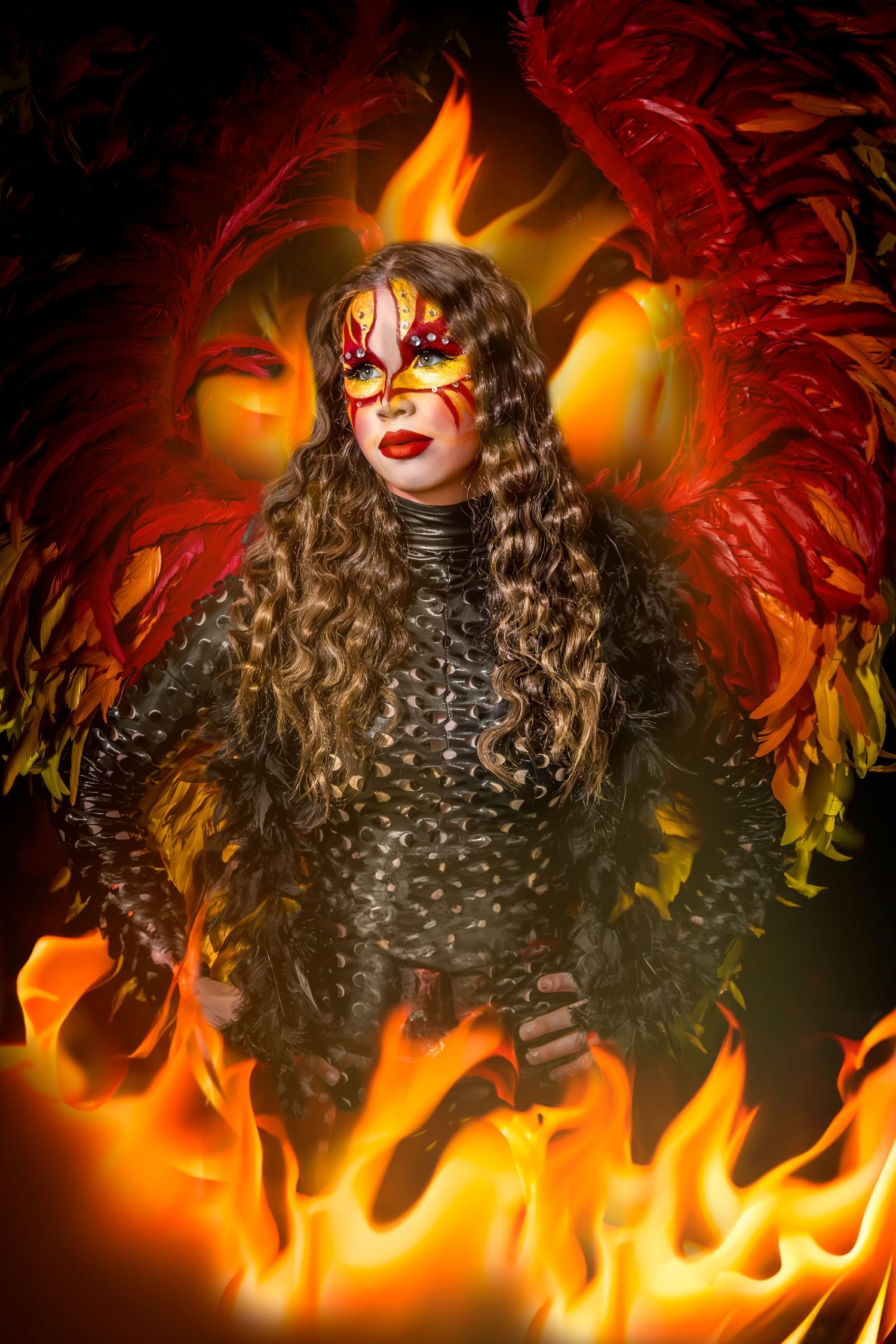 Gothic fashion portrait with flames and dramatic makeup against fiery orange background.