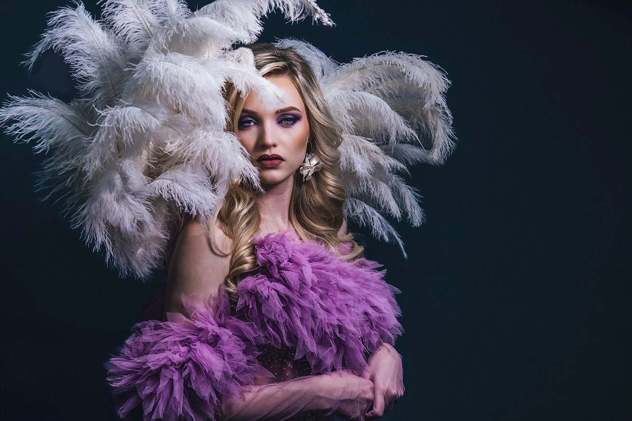 Glamorous sShowgirl portrait with white feathers and purple tulle against dark background. Vegas 2024
