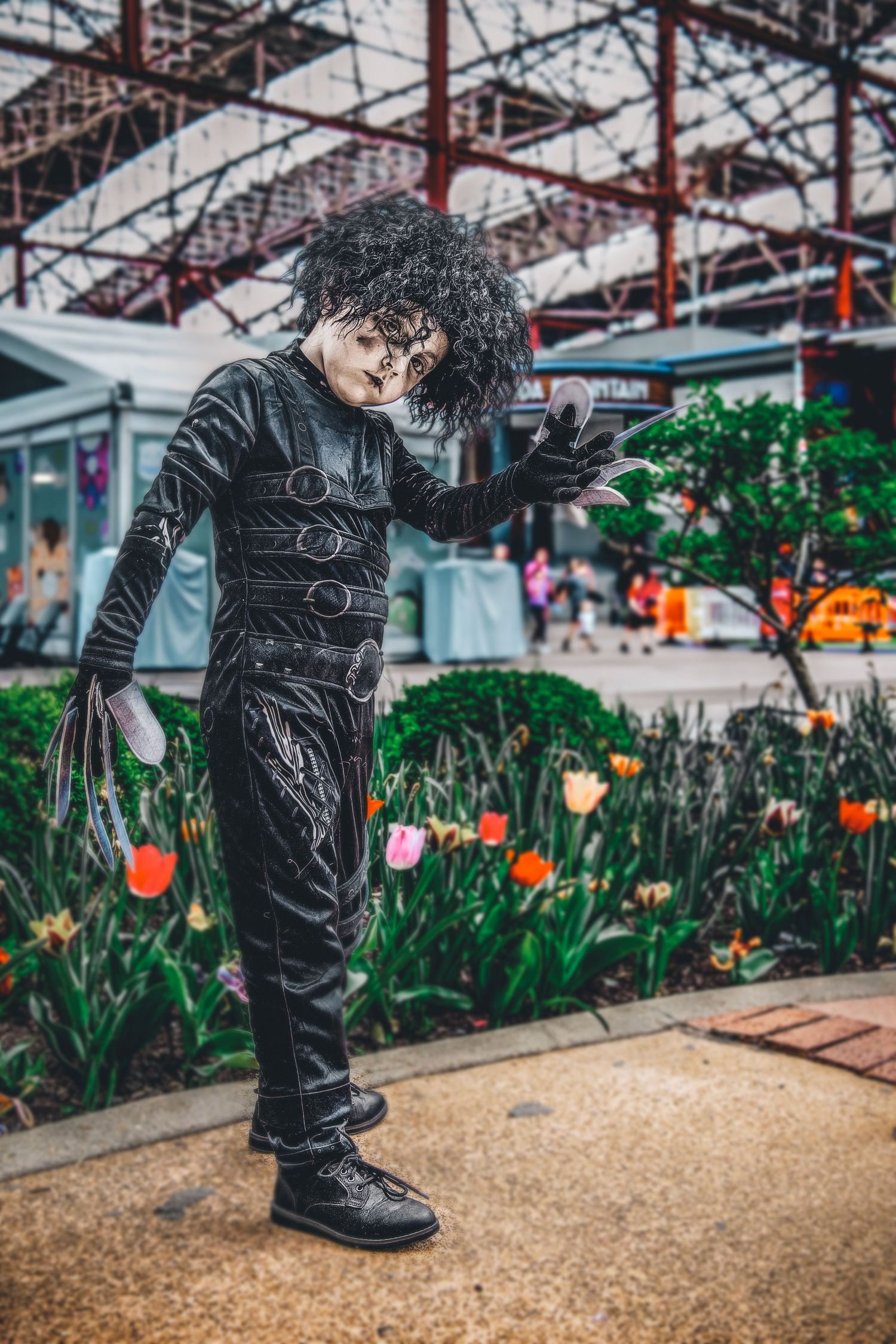 Figure in black outfit poses near colorful tulip garden under industrial architecture.