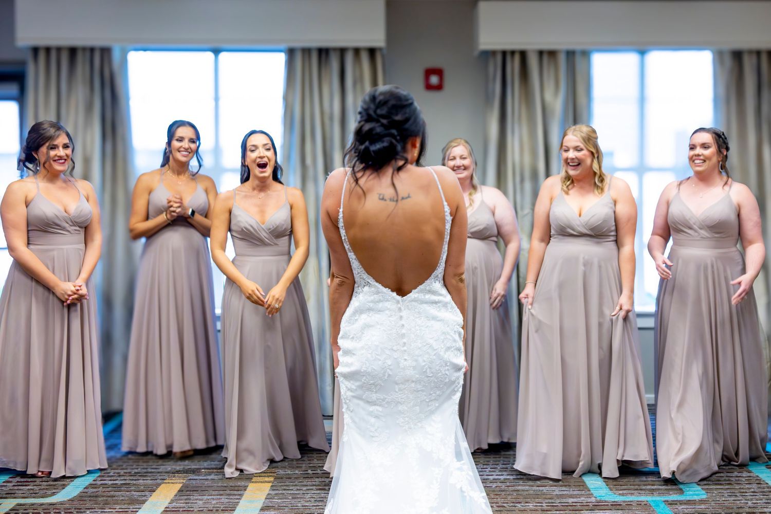 Bridesmaids wearing matching taupe colored dresses stand together in an elegant indoor setting.