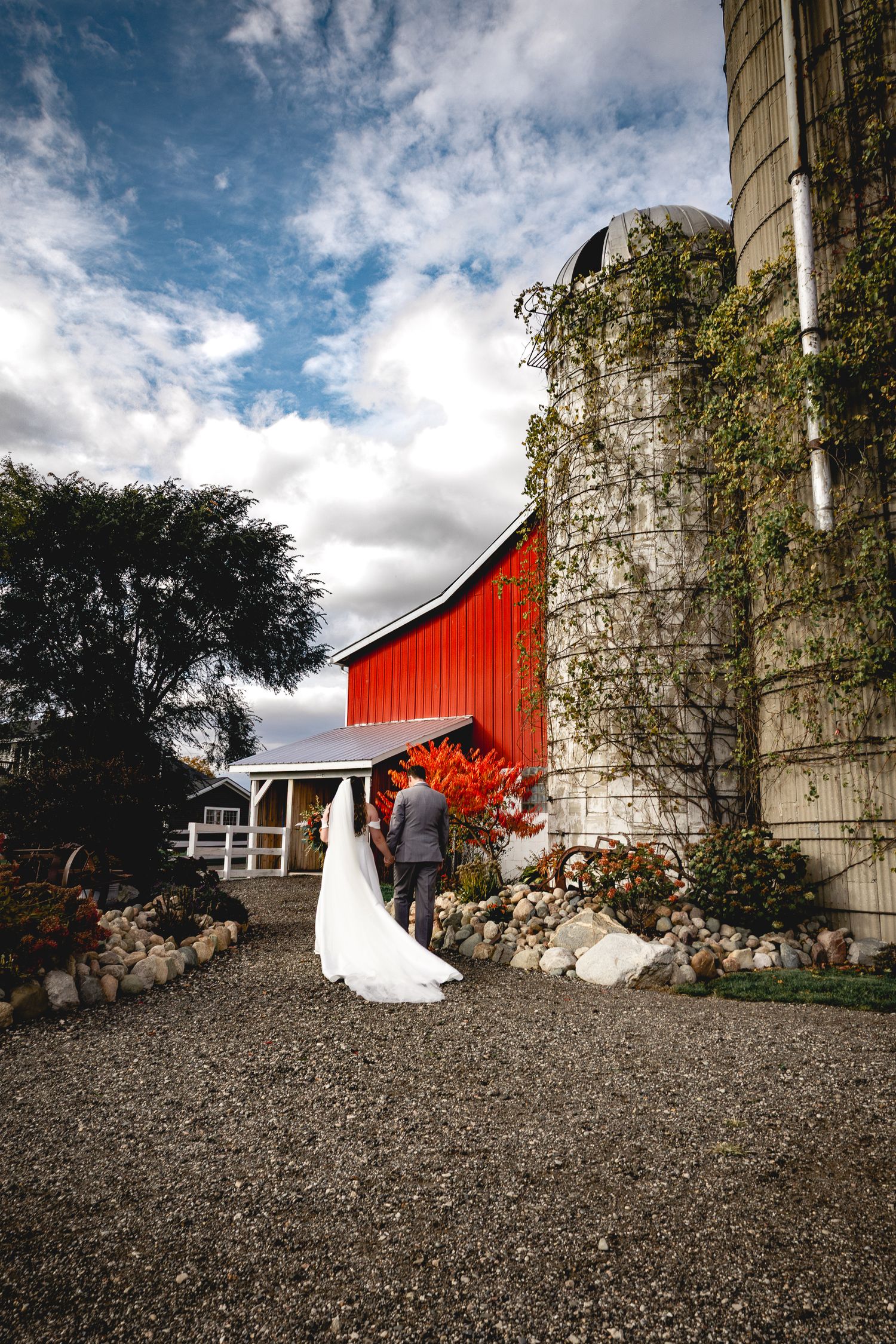 Wedding photo against red barn and white silo with ivy climbing the walls.