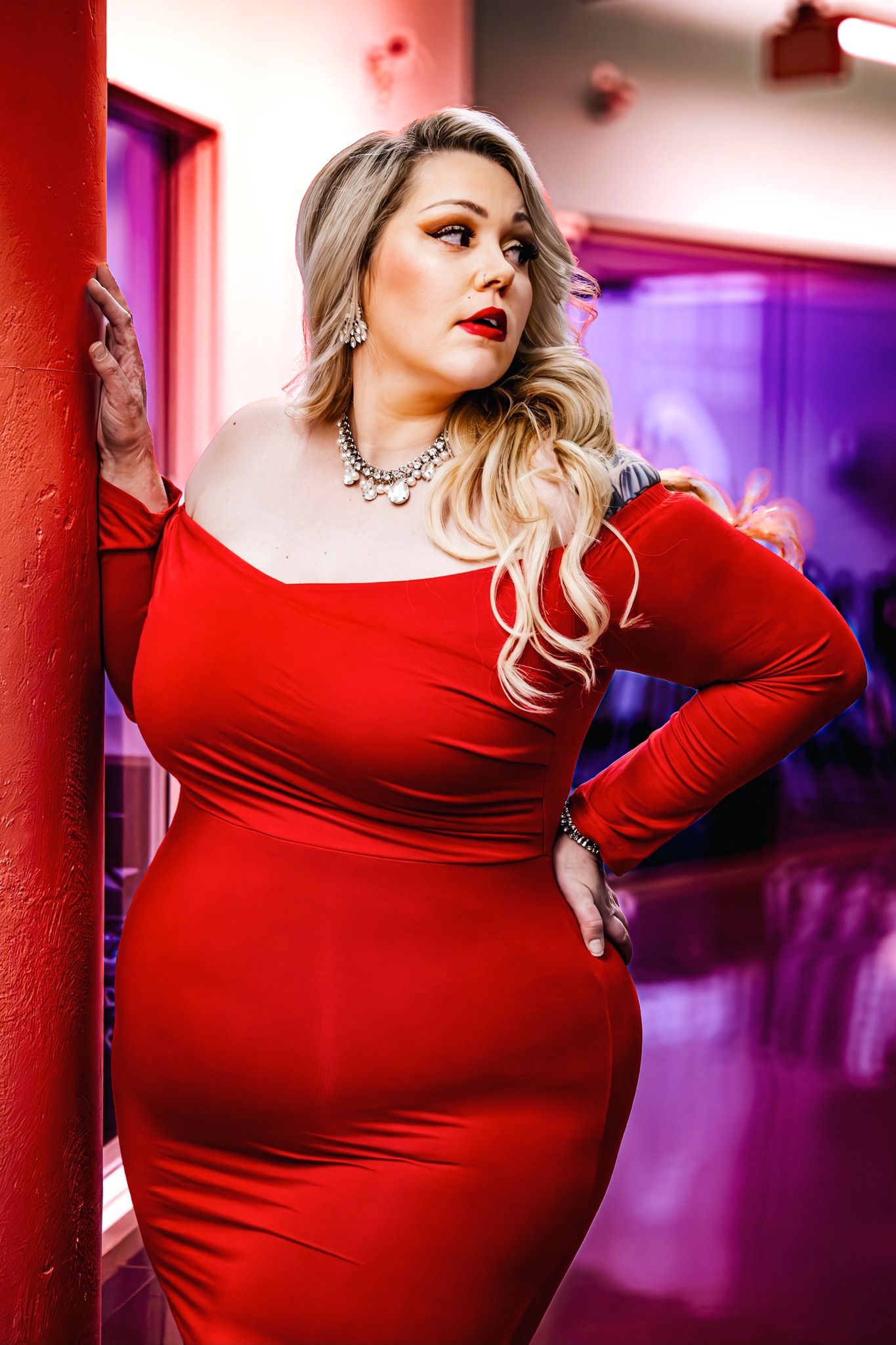 Model in red dress poses against colorful backdrop with dramatic lighting effects.