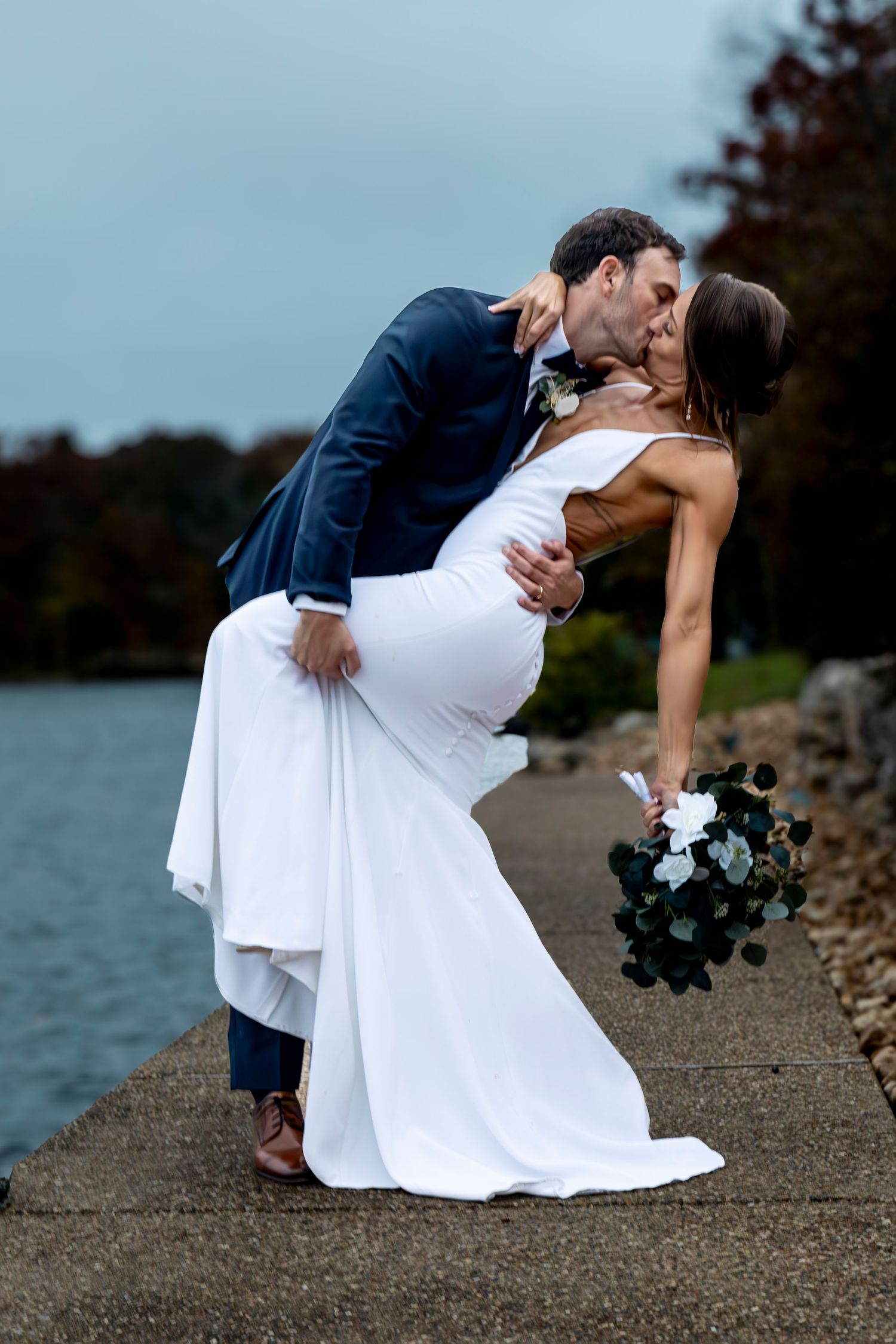 Classic wedding dip pose captured against waterfront backdrop.