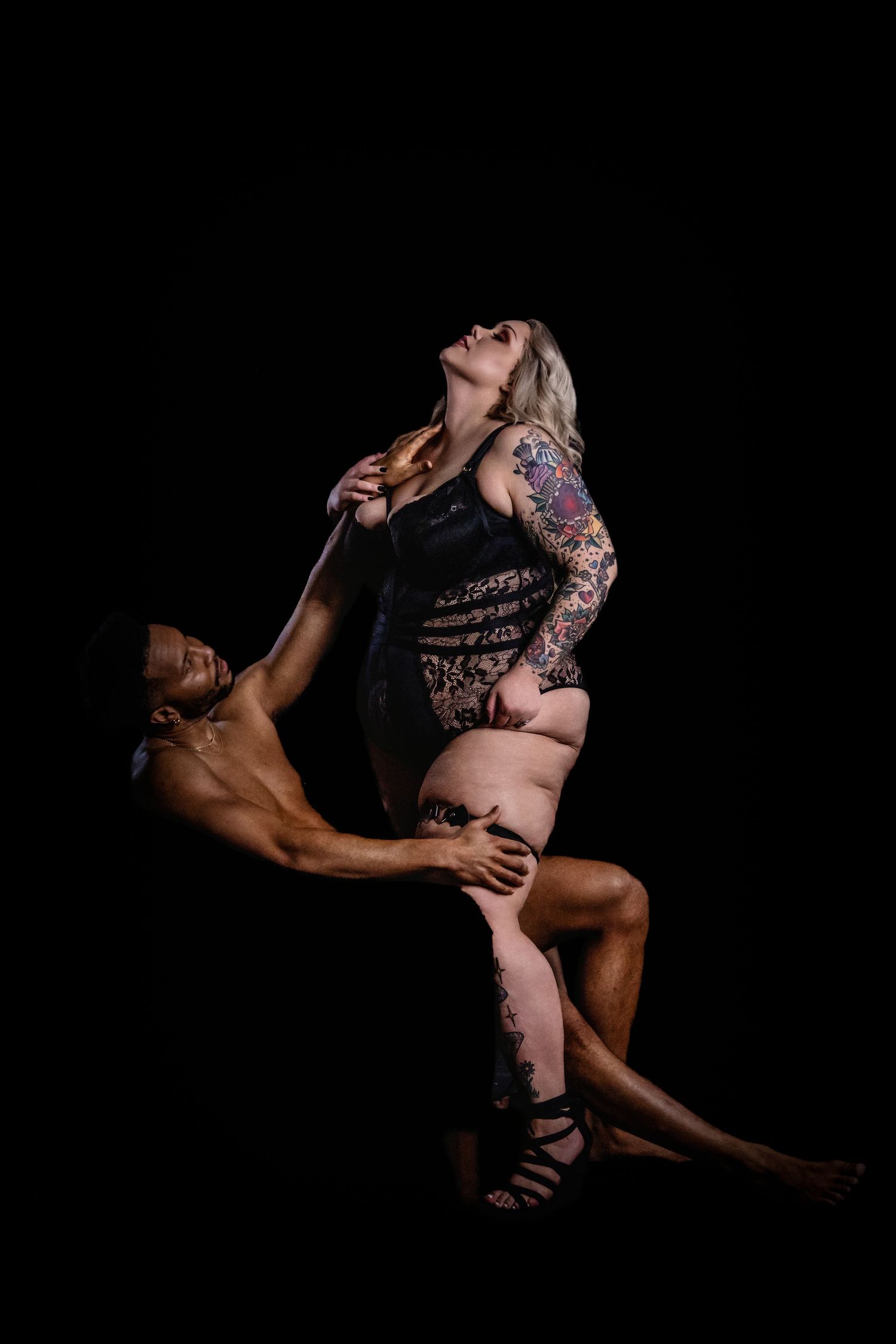 Artistic boudoir photograph with dramatic lighting against black background.