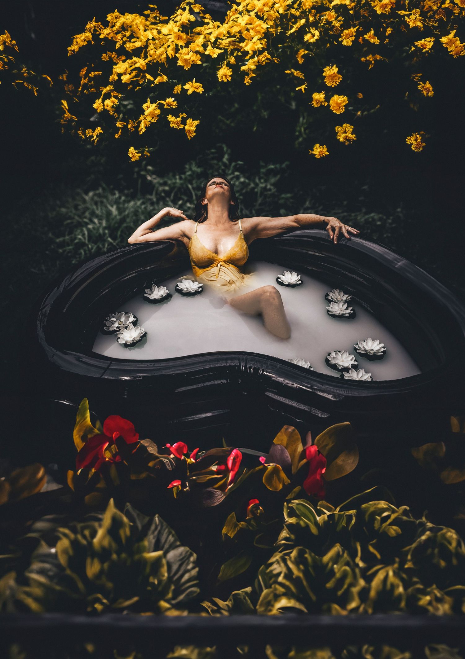 Outdoor milk bath photography in heart-shaped tub surrounded by yellow flowers and greenery.
