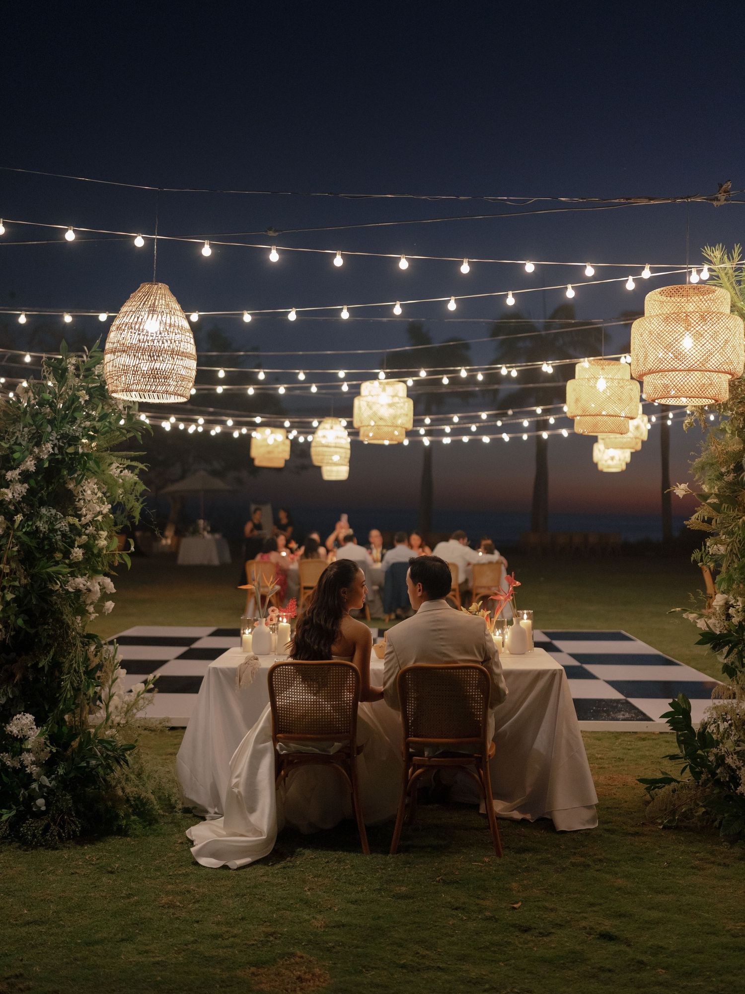 Outdoor evening reception with string lights and illuminated paper lanterns creating romantic ambiance.