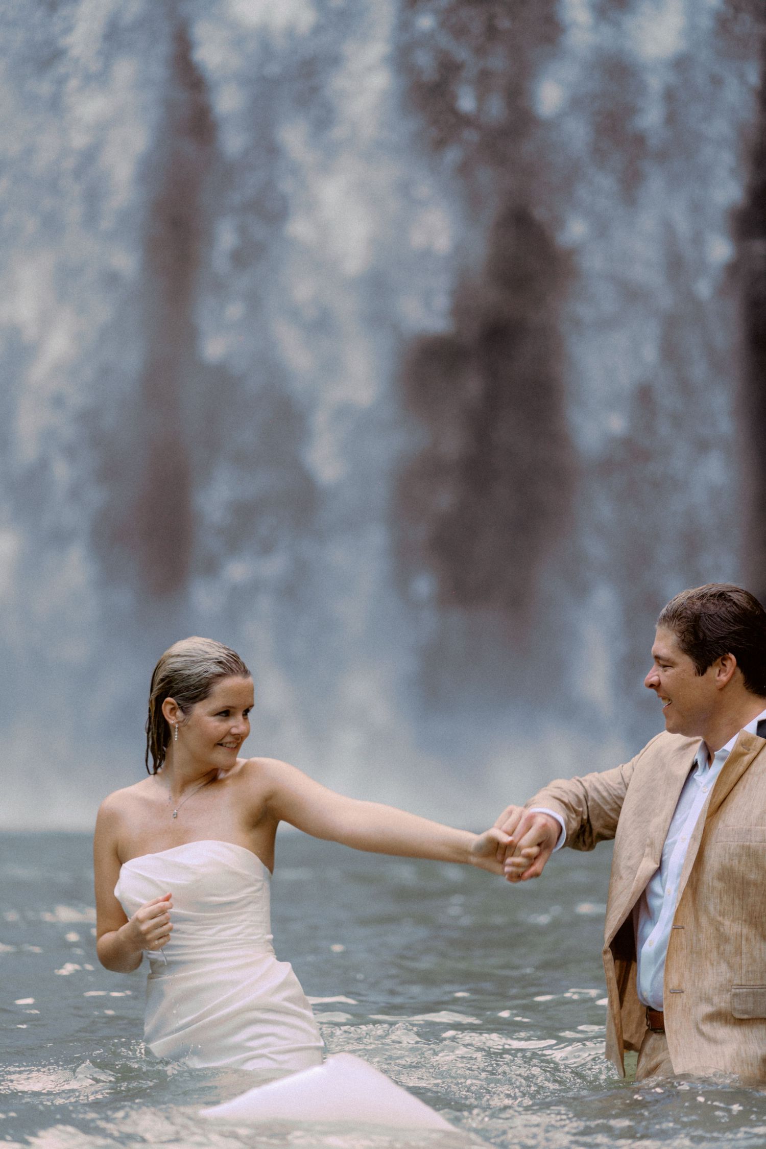 Two people dance and twirl in front of a cascading waterfall.