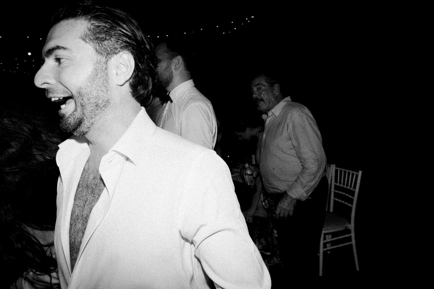 Wedding guests dance and celebrate on a dark dance floor during an evening reception.