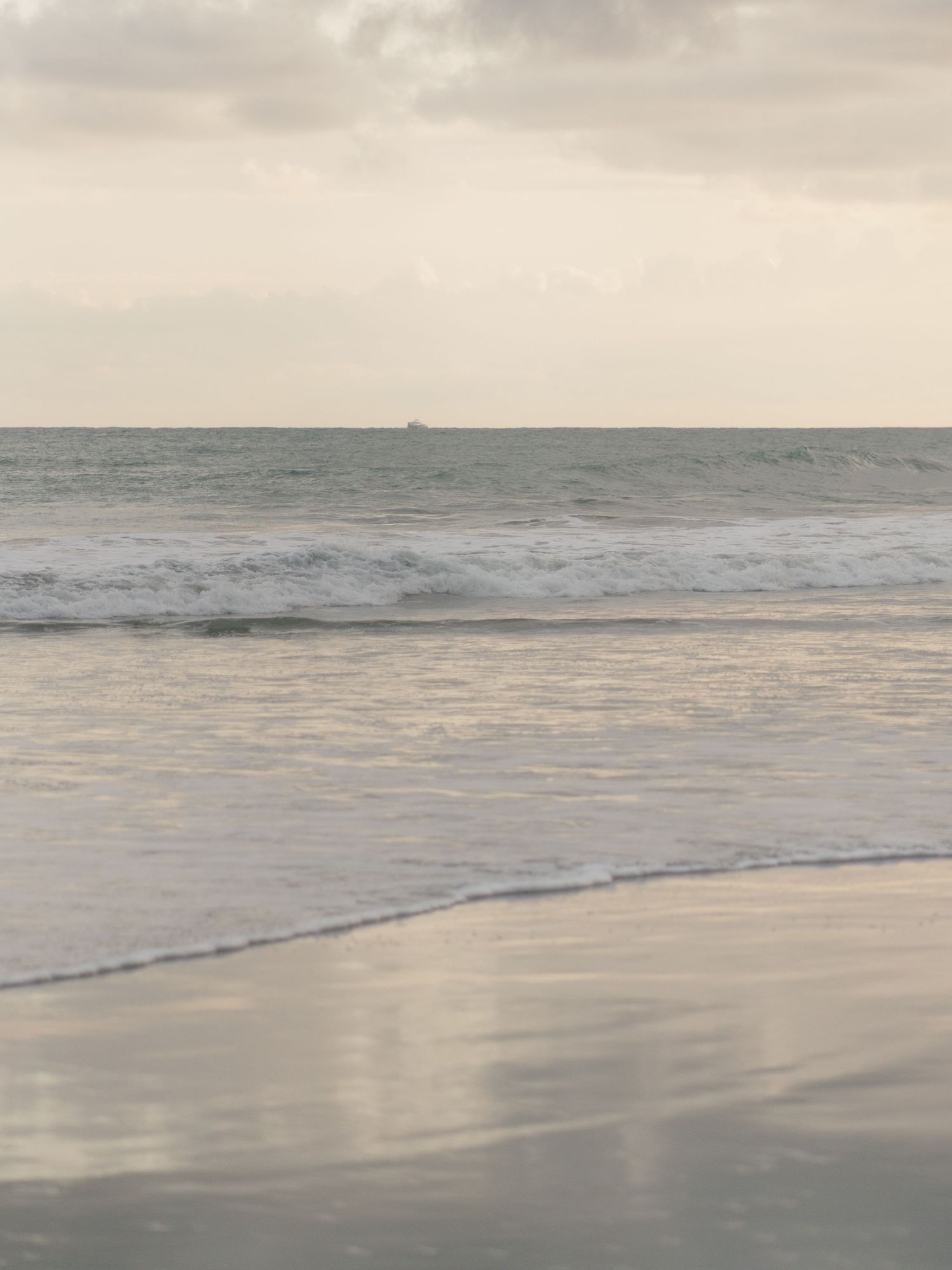 Tranquil beach scene at sunset with gentle waves rolling onto shore.