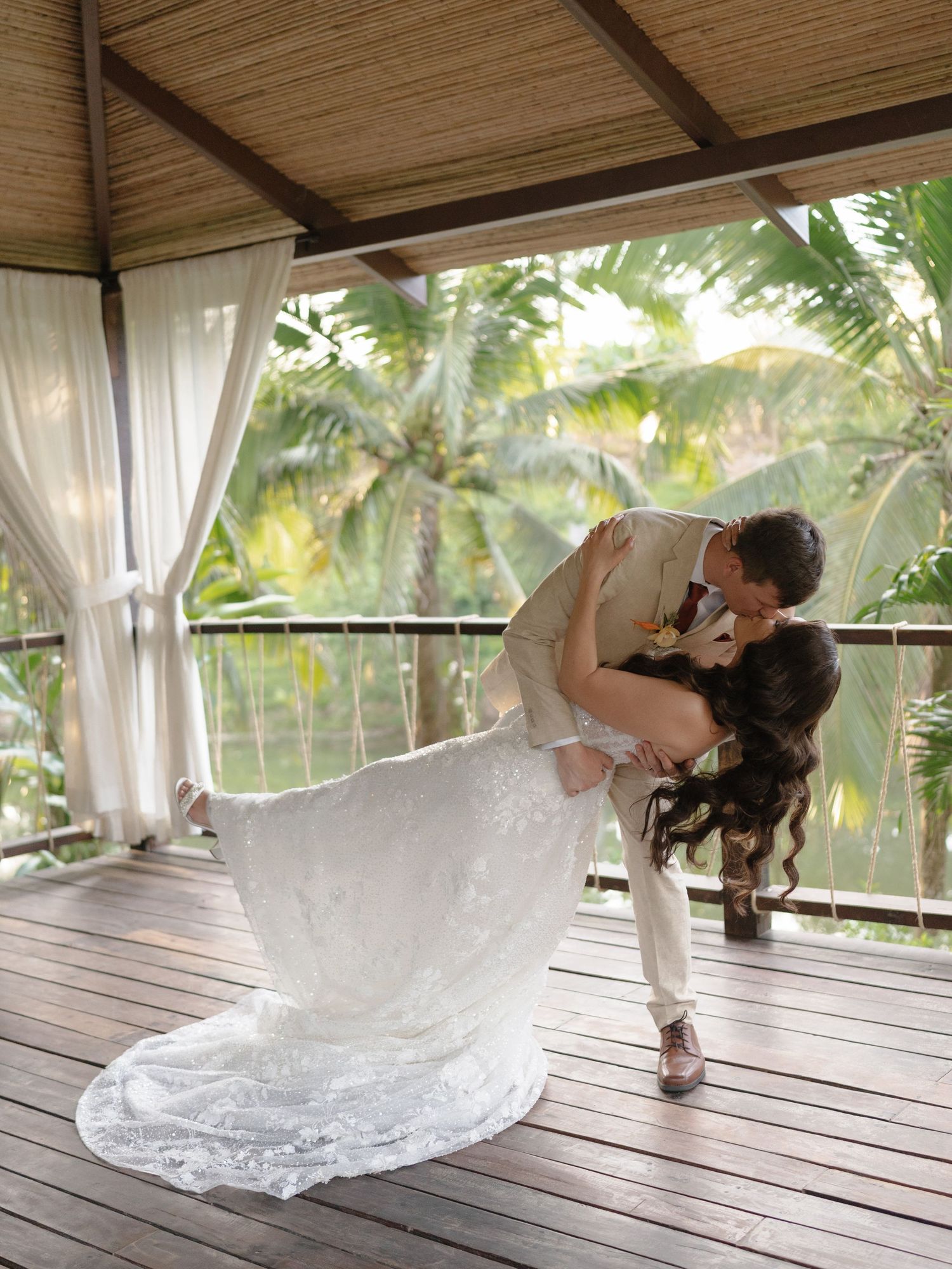 Romantic dance dip on a wooden deck surrounded by palm trees and white curtains.