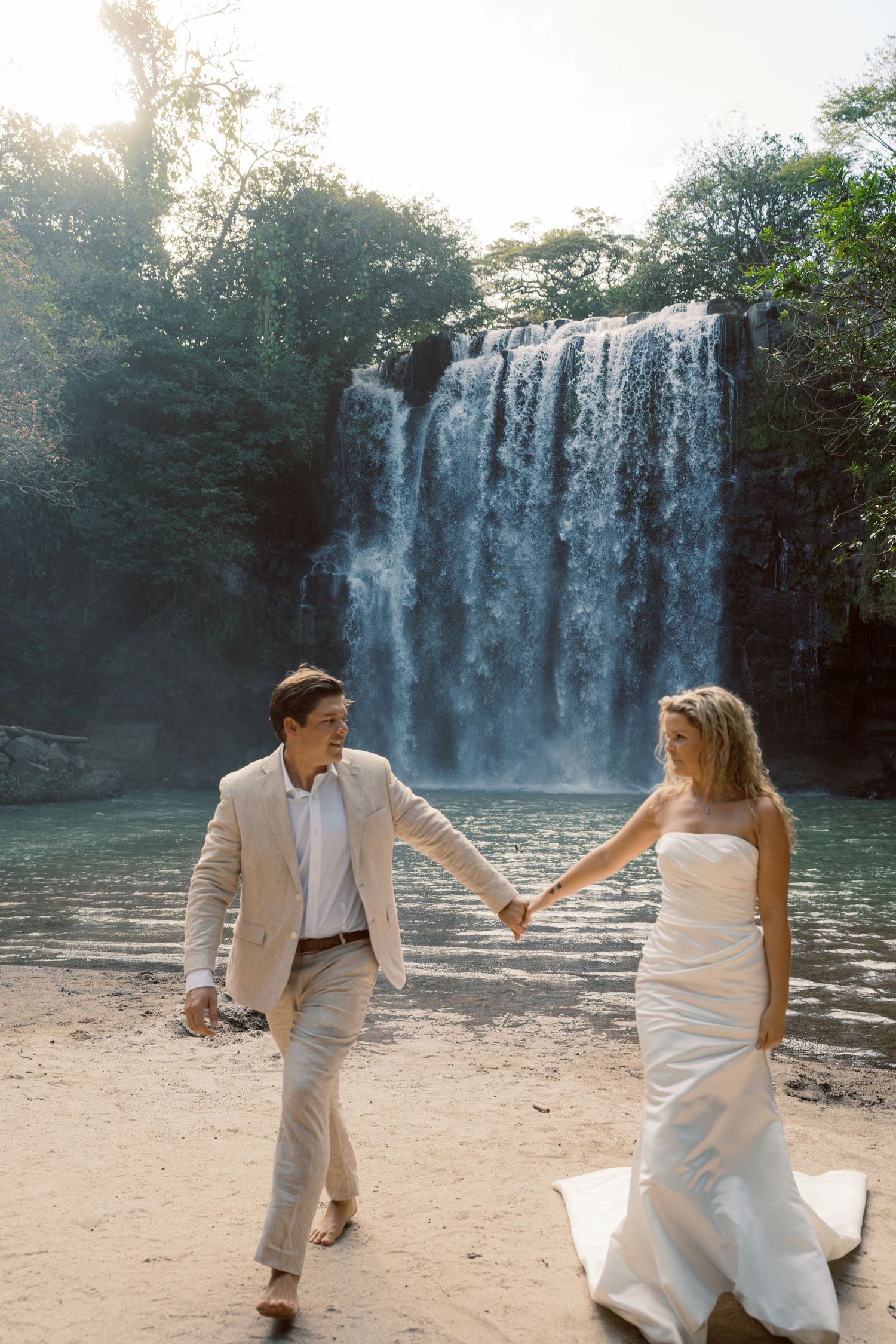 Playful dance movements captured on a sandy beach with a magnificent waterfall in the background.