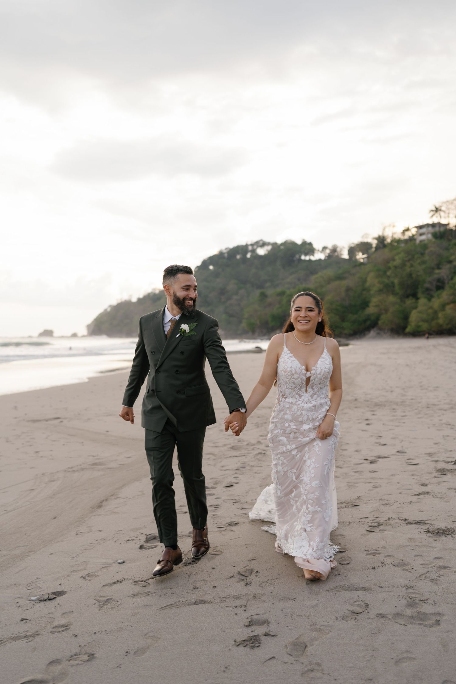 Couple running and laughing together on a sandy beach during sunset.