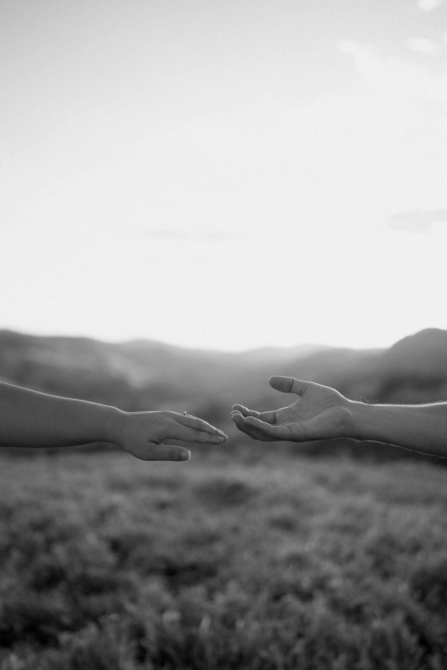 Silhouetted hands reach toward each other against a misty mountain landscape.