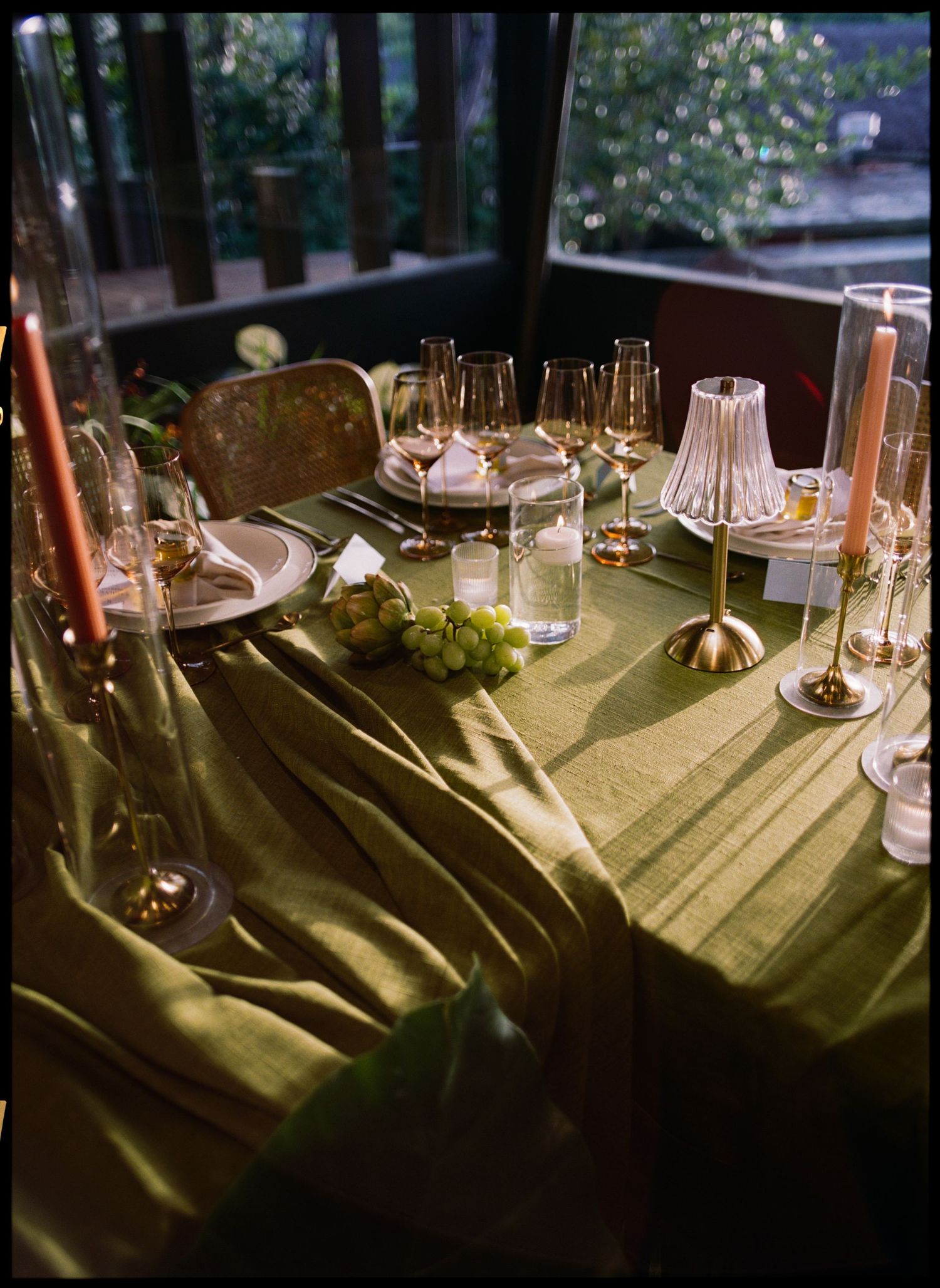 An elegant table setting with candles and glassware on olive green linens.