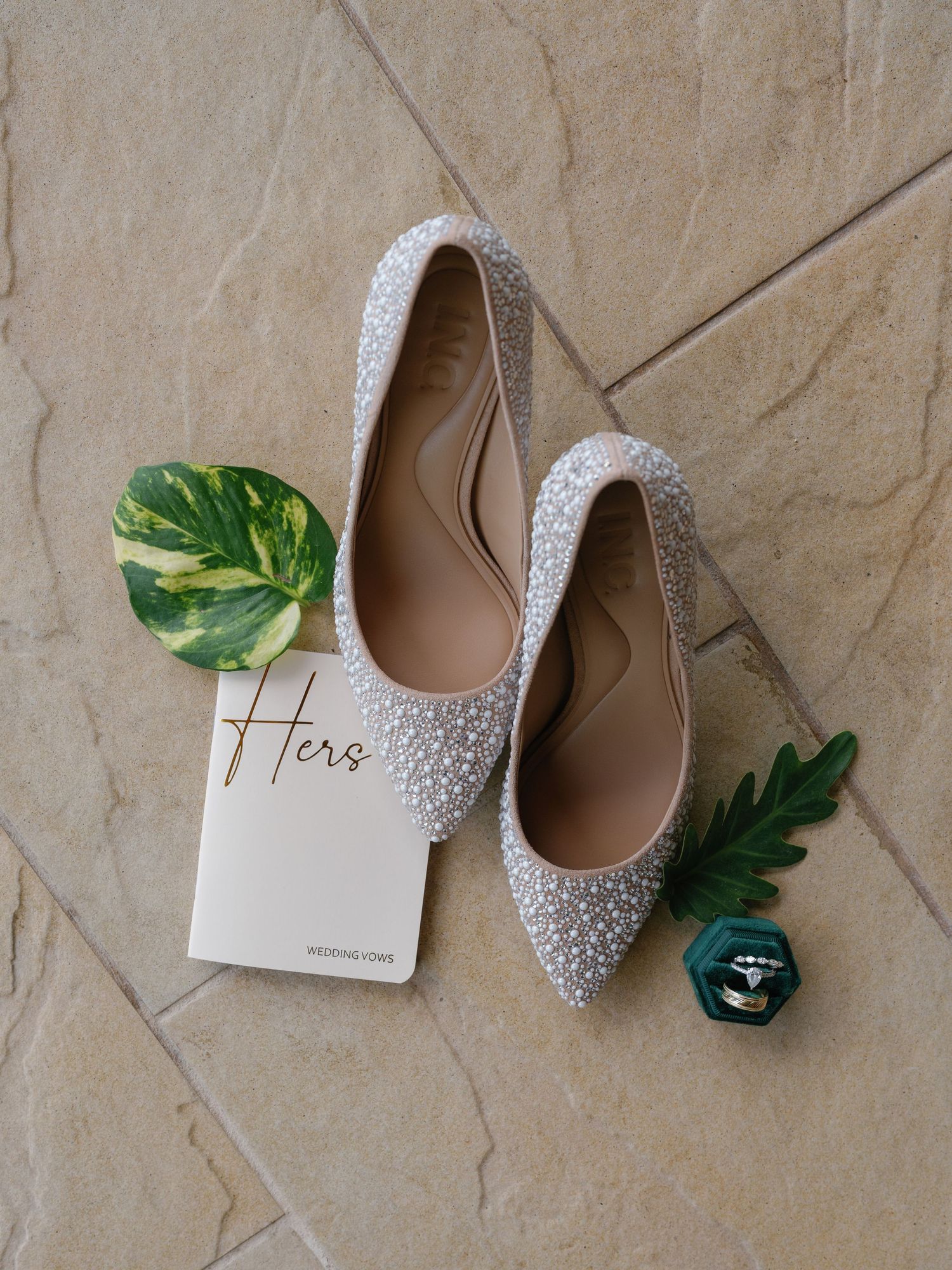 Sparkly wedding shoes and greenery styled on textured stone surface.