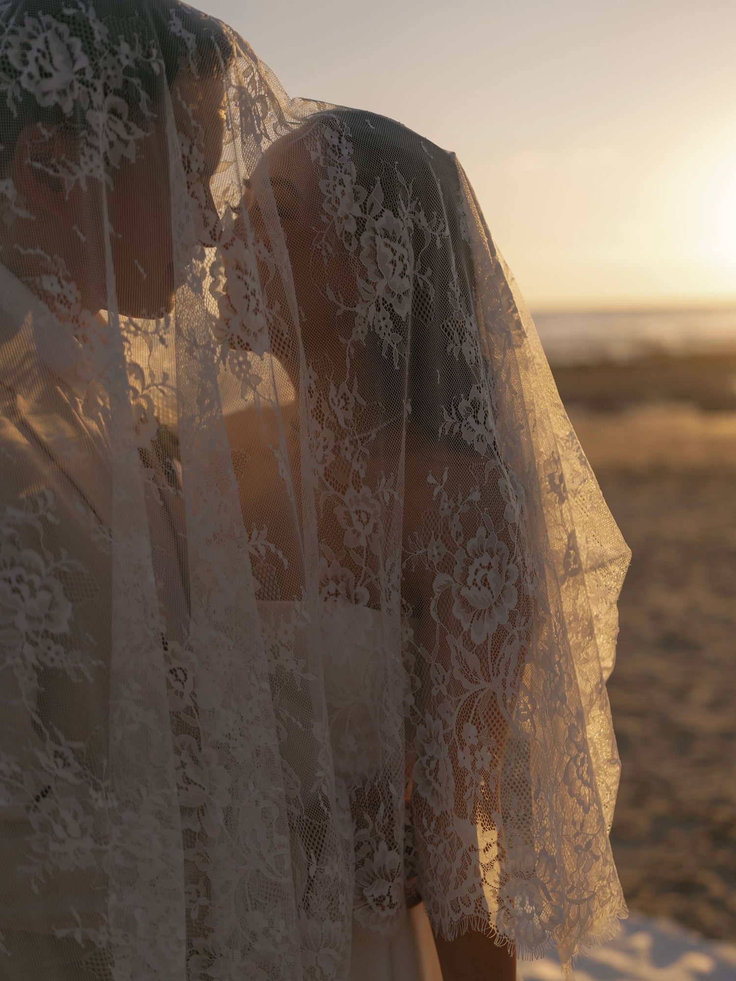 Delicate white lace veil flowing in golden sunset light against a desert landscape.