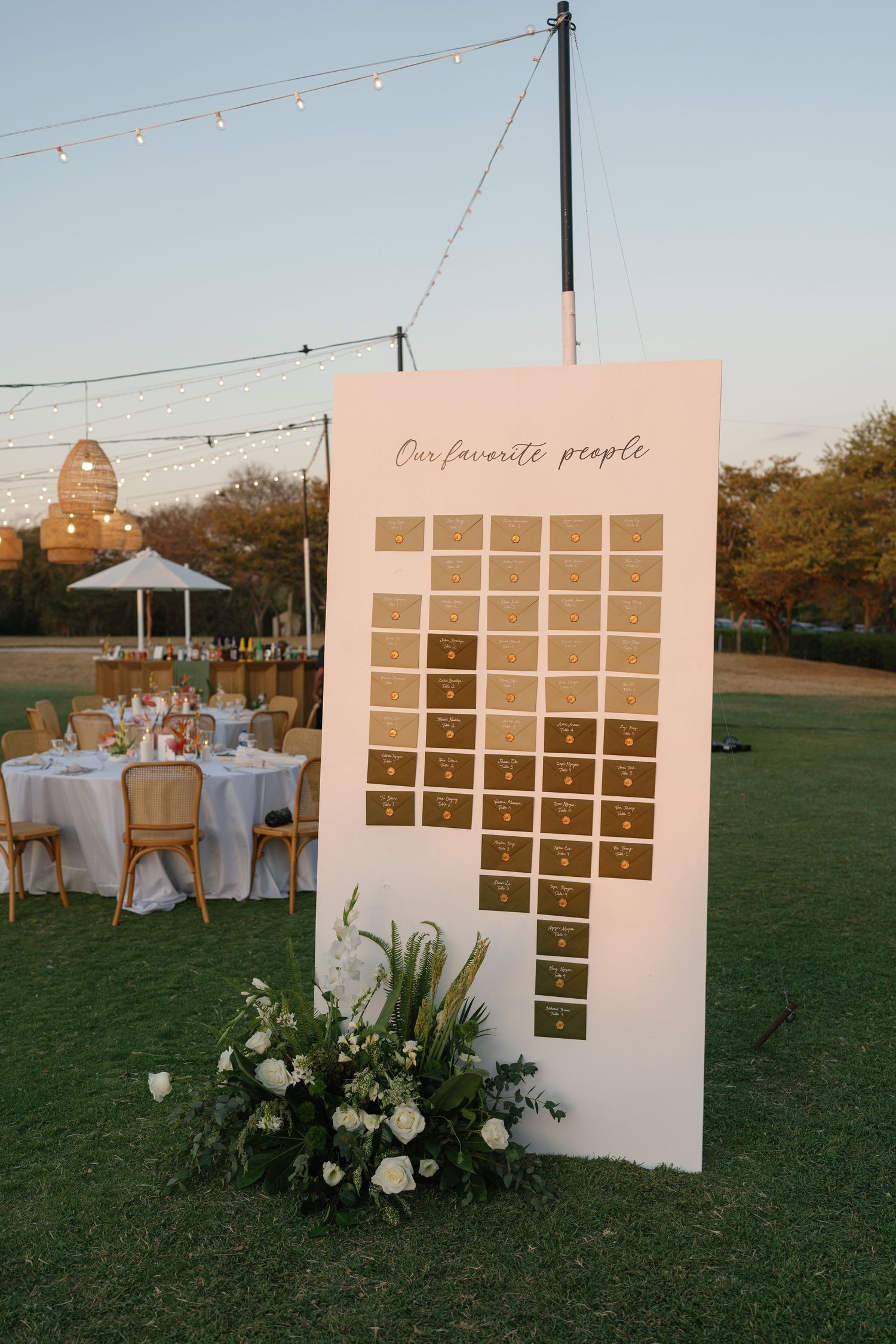 A wedding seating chart display with floral decorations and string lights in an outdoor garden setting.