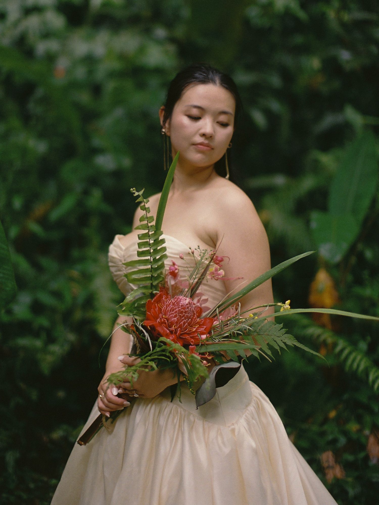 A bridal portrait featuring a tropical bouquet with red torch ginger and ferns in a garden setting.