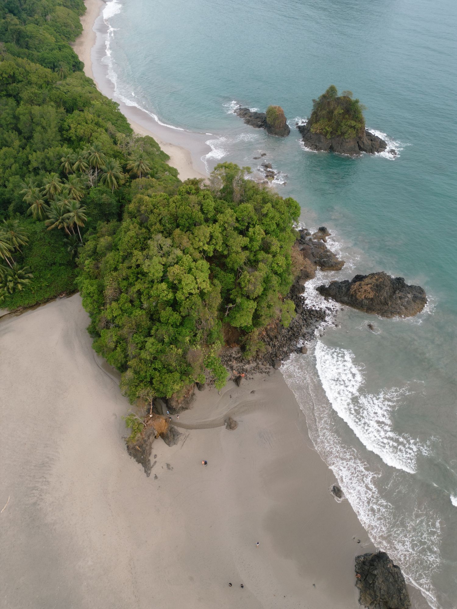 Aerial view of a tropical beach with lush greenery and rocky outcrops along the turquoise coastline.