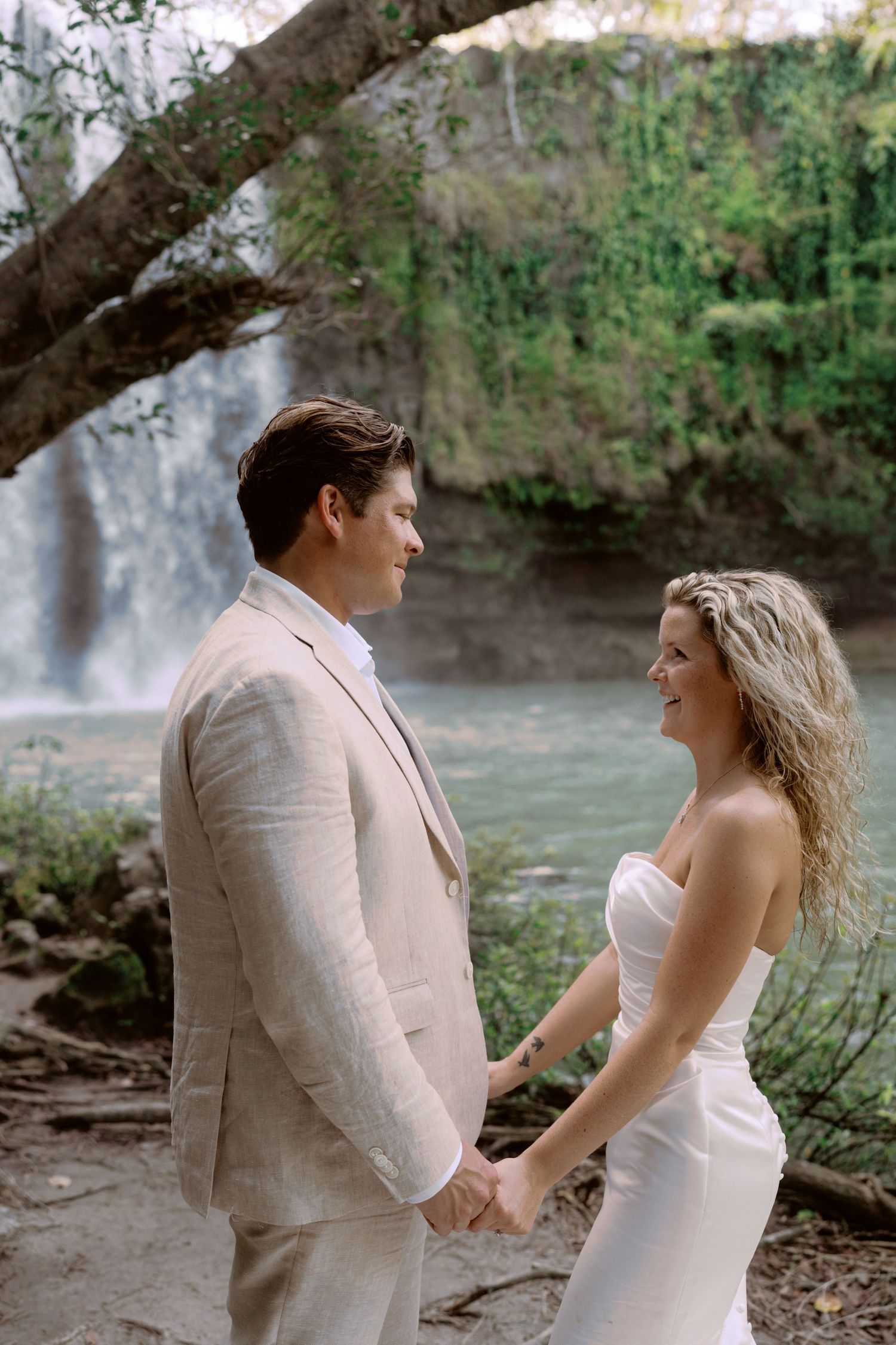 Wedding couple sharing tender moments against backdrop of flowing waterfall and natural scenery.
