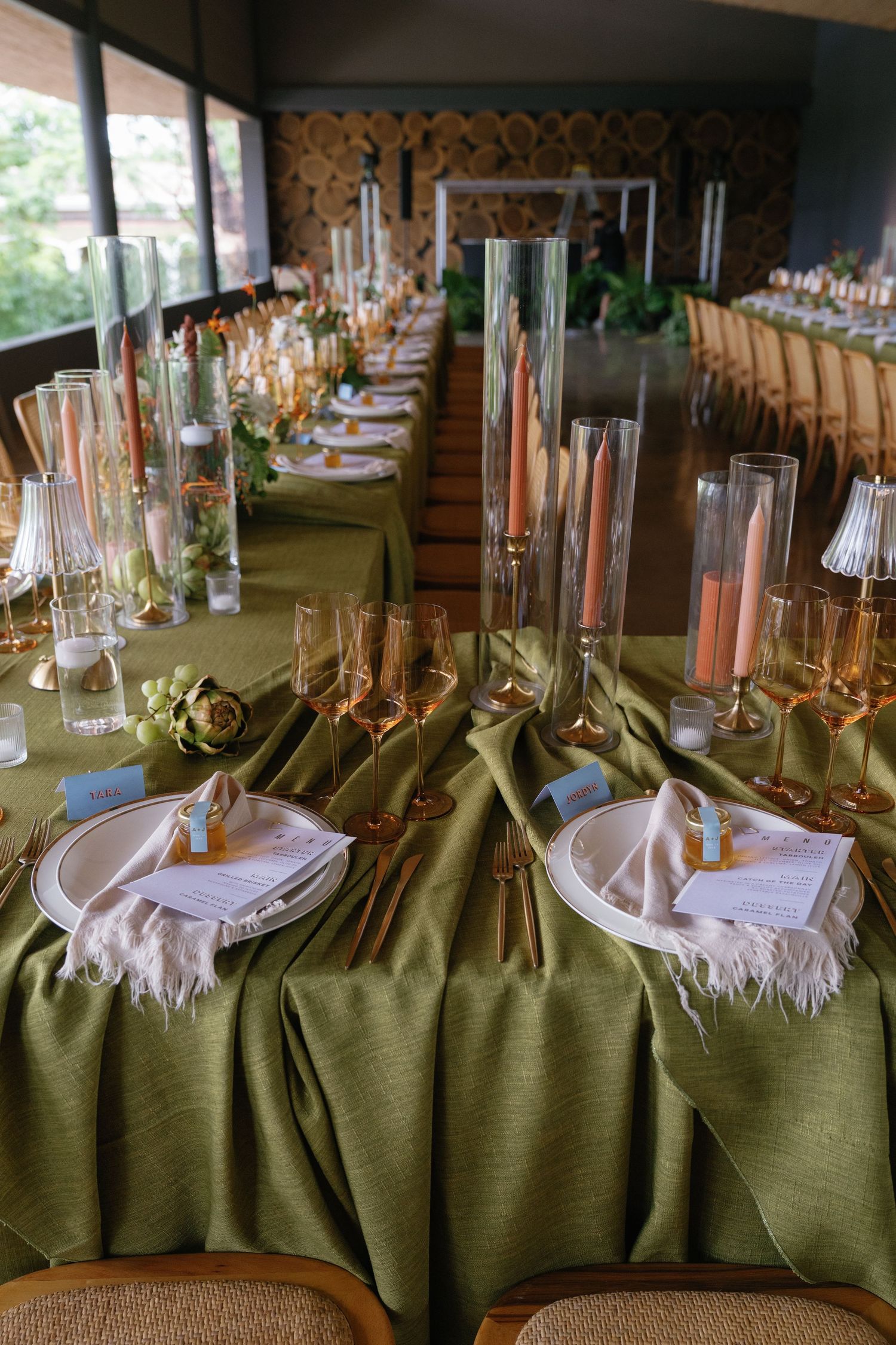 A formal dining table set with olive green linens and tall glass candleholders.