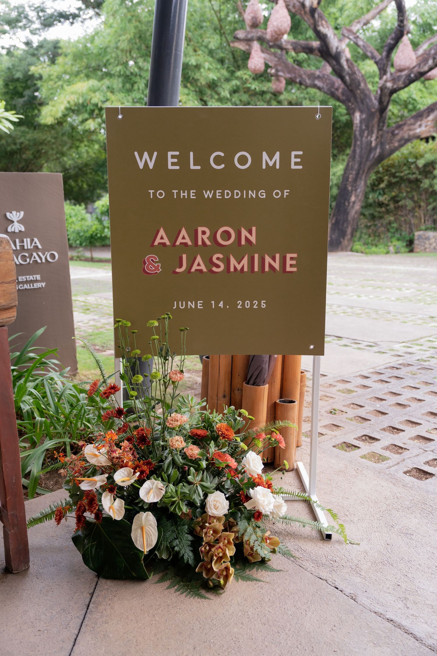 Elegant brown wedding welcome signs with floral arrangements displayed outdoors on stone pavement.
