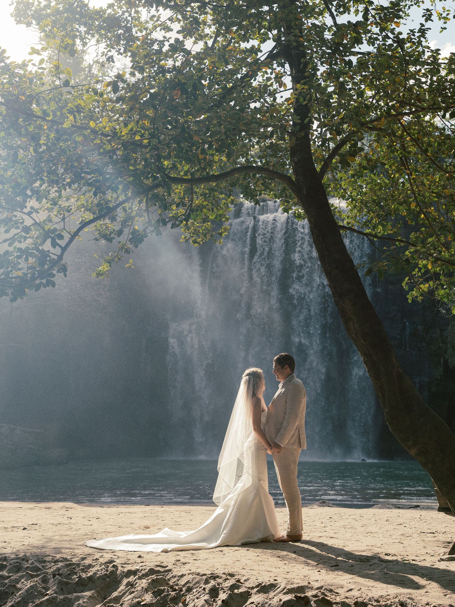 Romantic waterfall photoshoot with couple in elegant attire during golden hour.