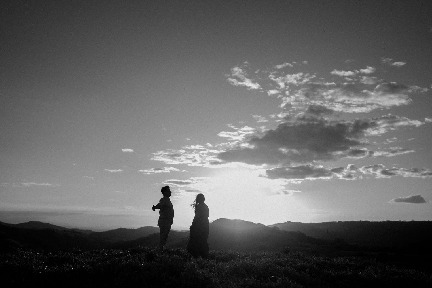 Dark silhouettes stand against a dramatic sunset sky over mountain ridges.