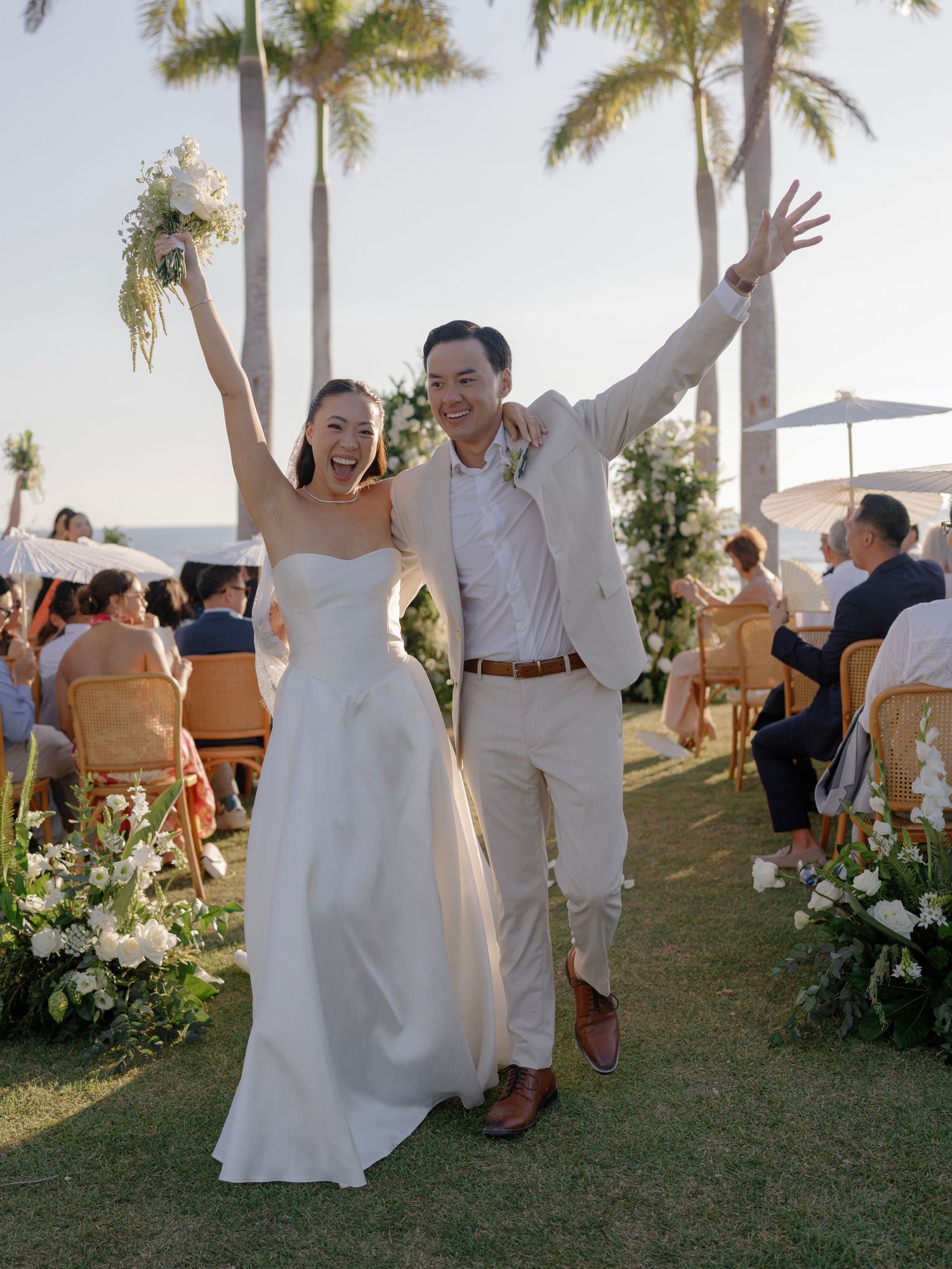 Wedding celebration on a palm-lined lawn with guests in white and formal attire.