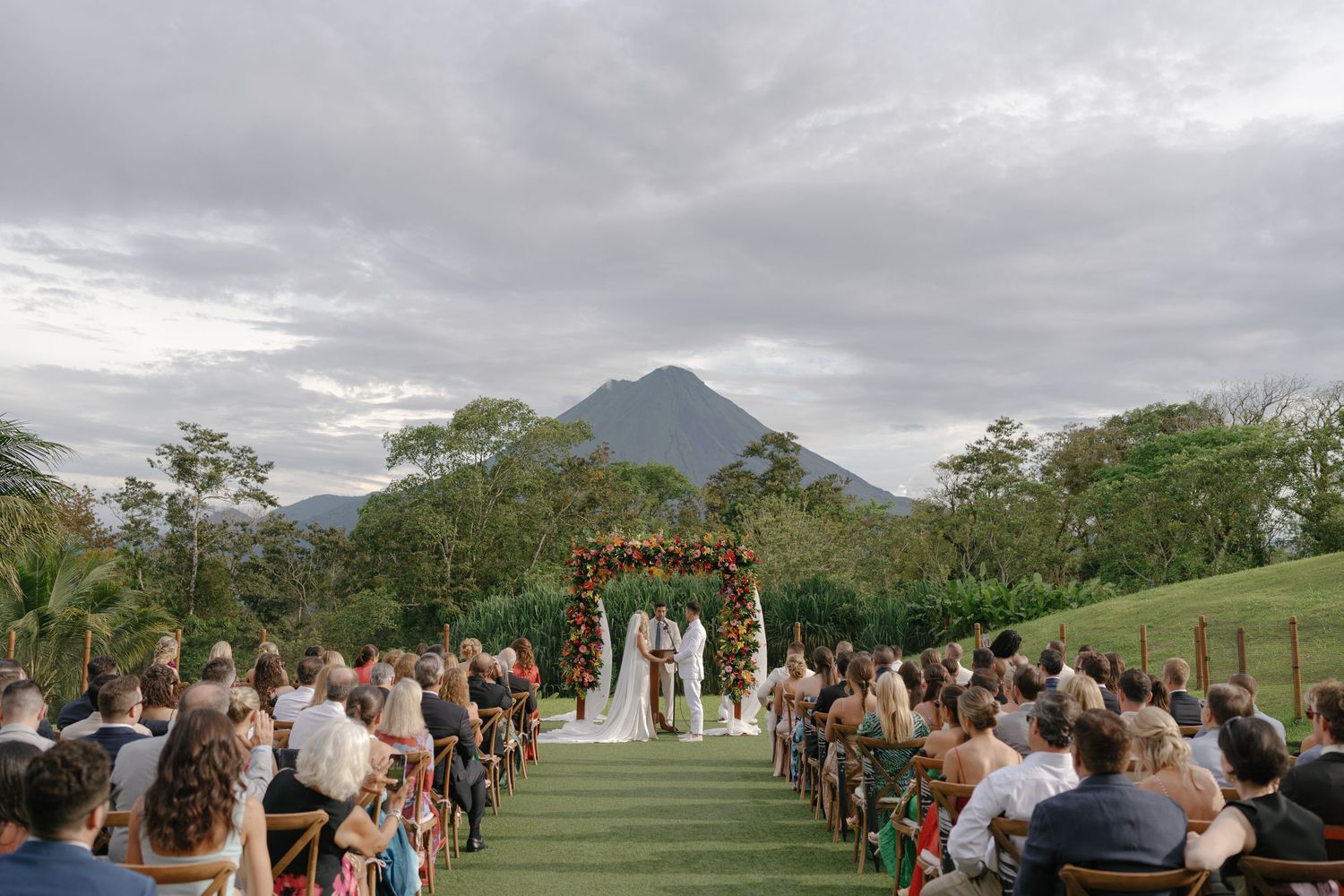Wedding guests seated in rows on a grassy hillside with volcanic mountain vista.